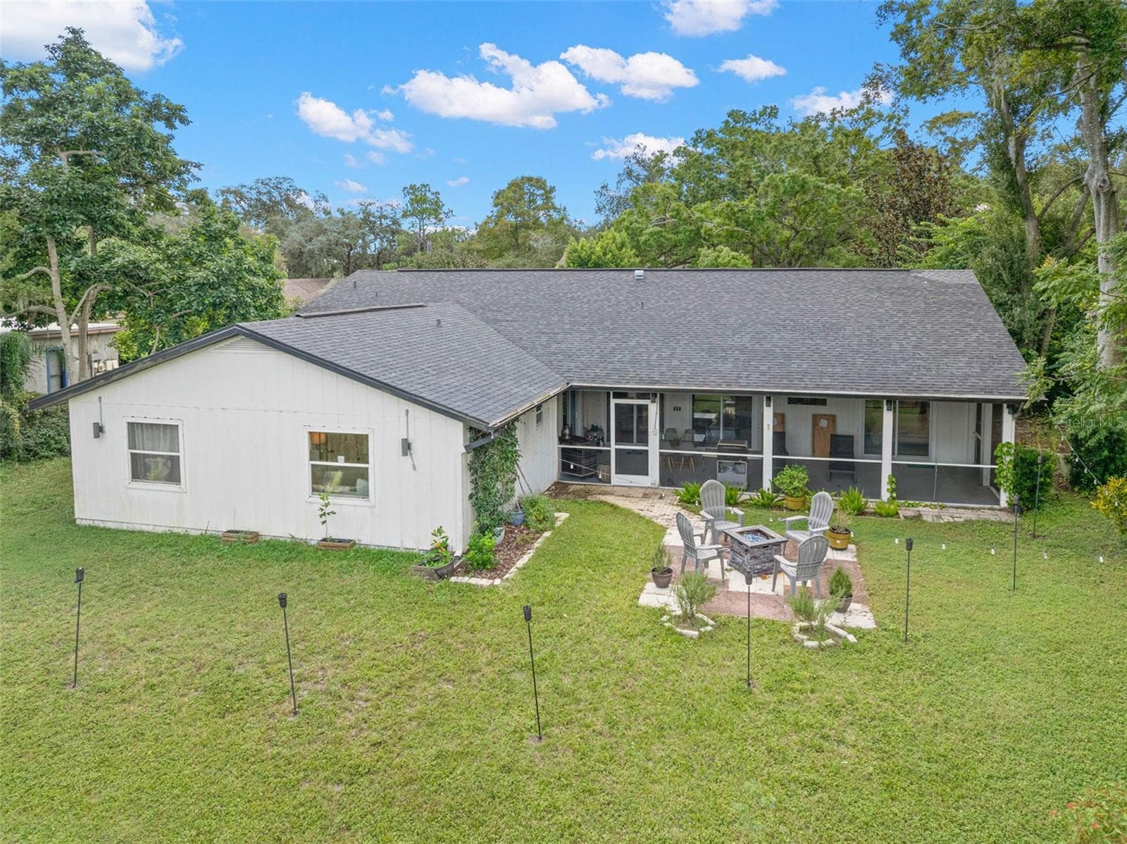 An aerial perspective showcases the home's expansive backyard, mature surrounding trees, and impressive screened porch extending across the rear of the residence. A dedicated patio and fire pit area adds another inviting outdoor gathering space, with plenty of lawn to enjoy. - 3013 GRAHAM LN, TAMPA