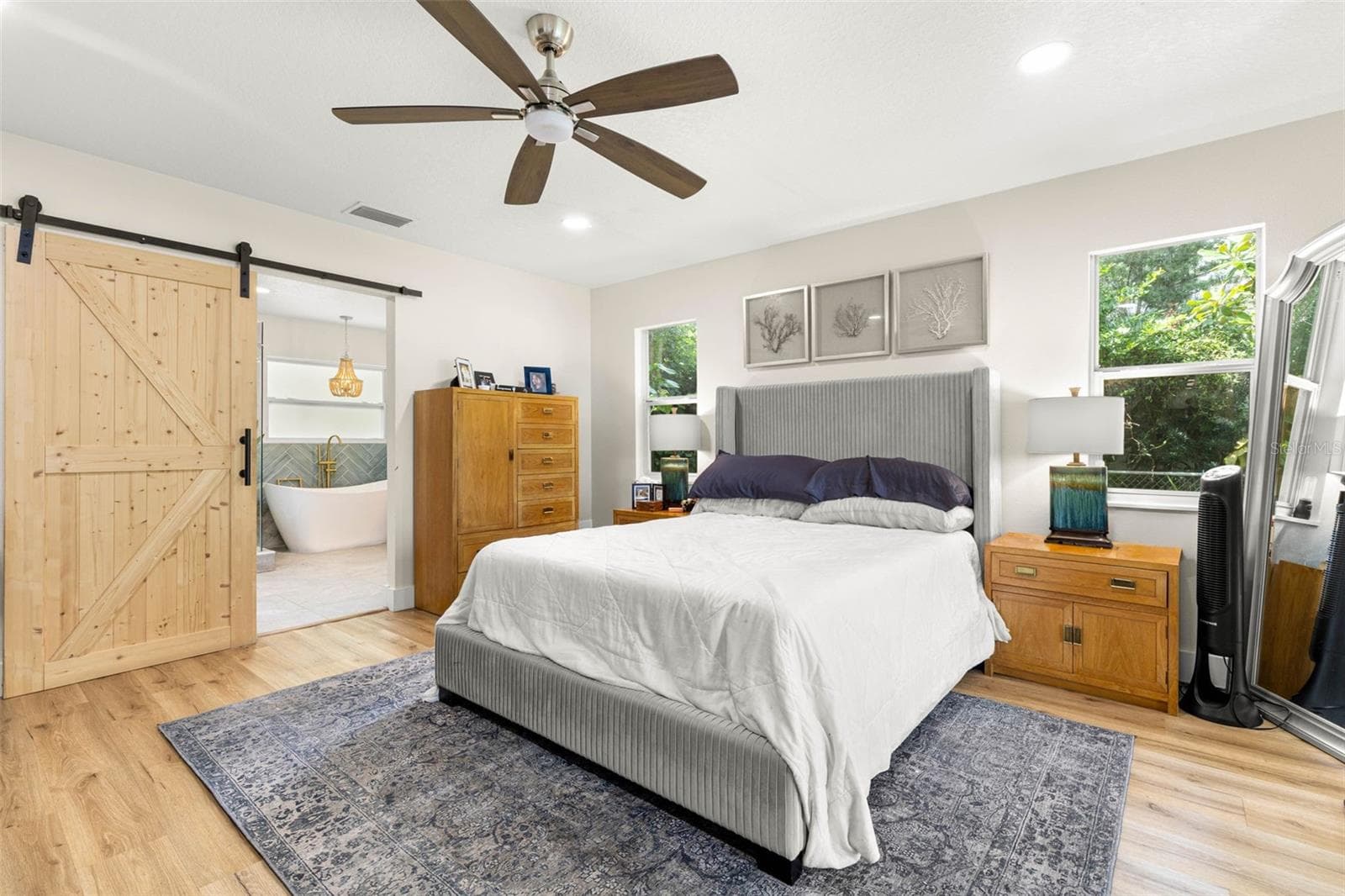 The inviting primary suite features beautiful wood-look luxury vinyl flooring, recessed lighting, a contemporary ceiling fan, and windows overlooking the greenery outside. A rustic sliding barn door adds architectural character while opening to the beautifully appointed ensuite bathroom. - 3013 GRAHAM LN, TAMPA