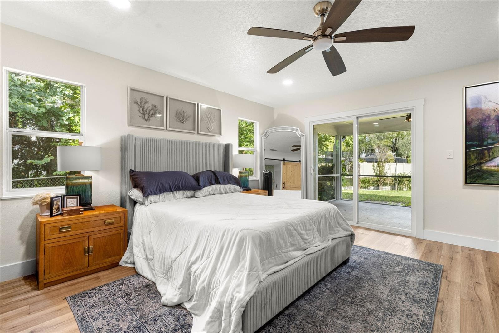The primary bedroom offers a relaxing retreat with abundant natural light from multiple windows and sliding glass doors that open directly to the screened porch. Enjoy easy access to the outdoors, wood-look luxury vinyl flooring, and a contemporary ceiling fan. - 3013 GRAHAM LN, TAMPA