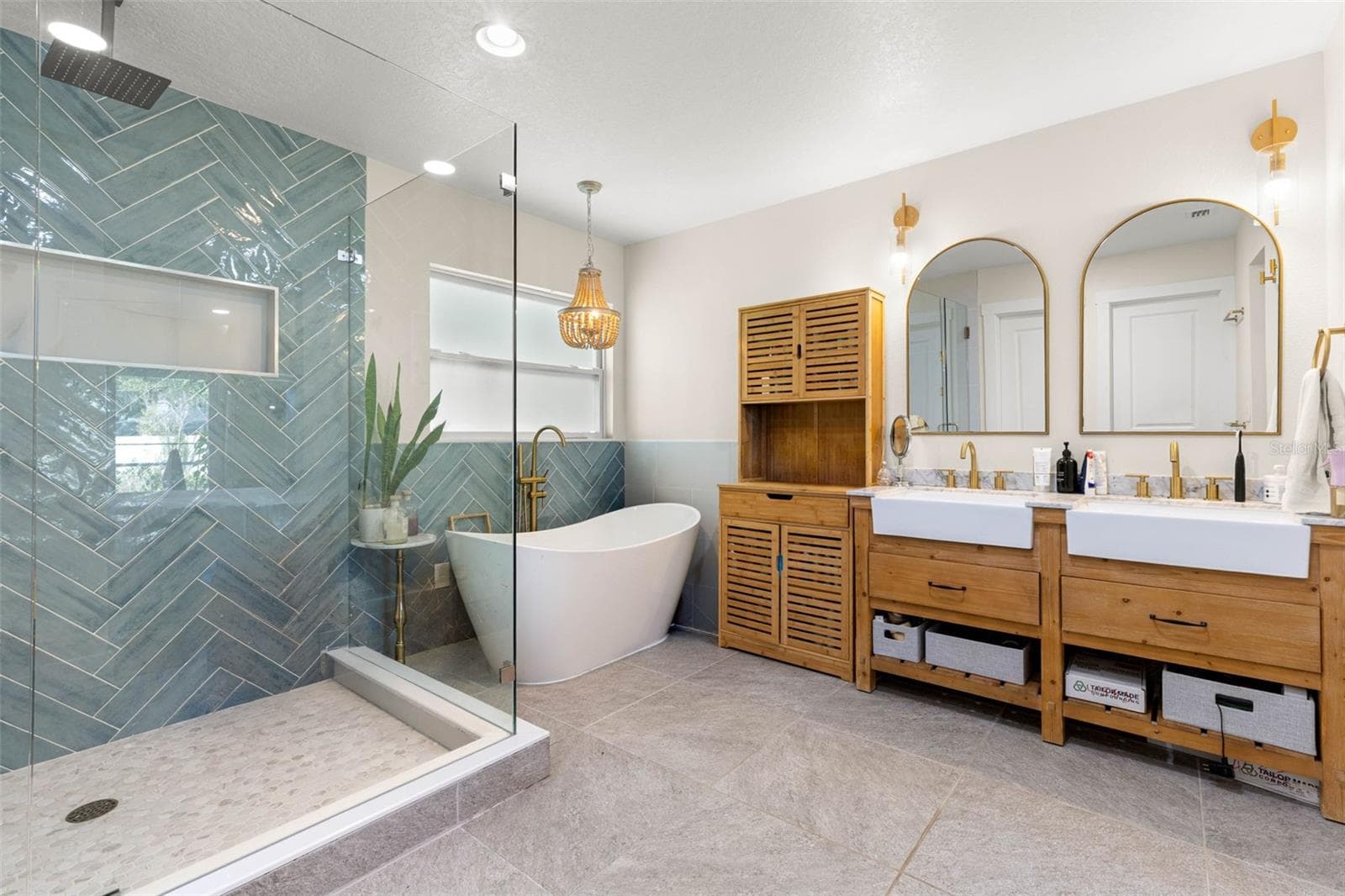 The stunning primary ensuite offers a spa-inspired retreat featuring a freestanding soaking tub, an oversized walk-in shower with frameless glass enclosure, dramatic blue-green herringbone tile, and dual farmhouse-style vessel sinks set atop warm wood vanities. Gold fixtures, arched mirrors, and coordinating sconces complete this beautifully designed bathroom. - 3013 GRAHAM LN, TAMPA