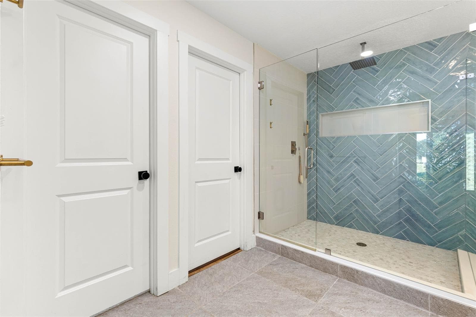 The primary bathroom's oversized walk-in shower features a frameless glass enclosure, striking blue-green herringbone tile, a rainfall showerhead, built-in recessed niche, and a pebble-style tile floor. A beautiful combination of contemporary design and everyday functionality. - 3013 GRAHAM LN, TAMPA