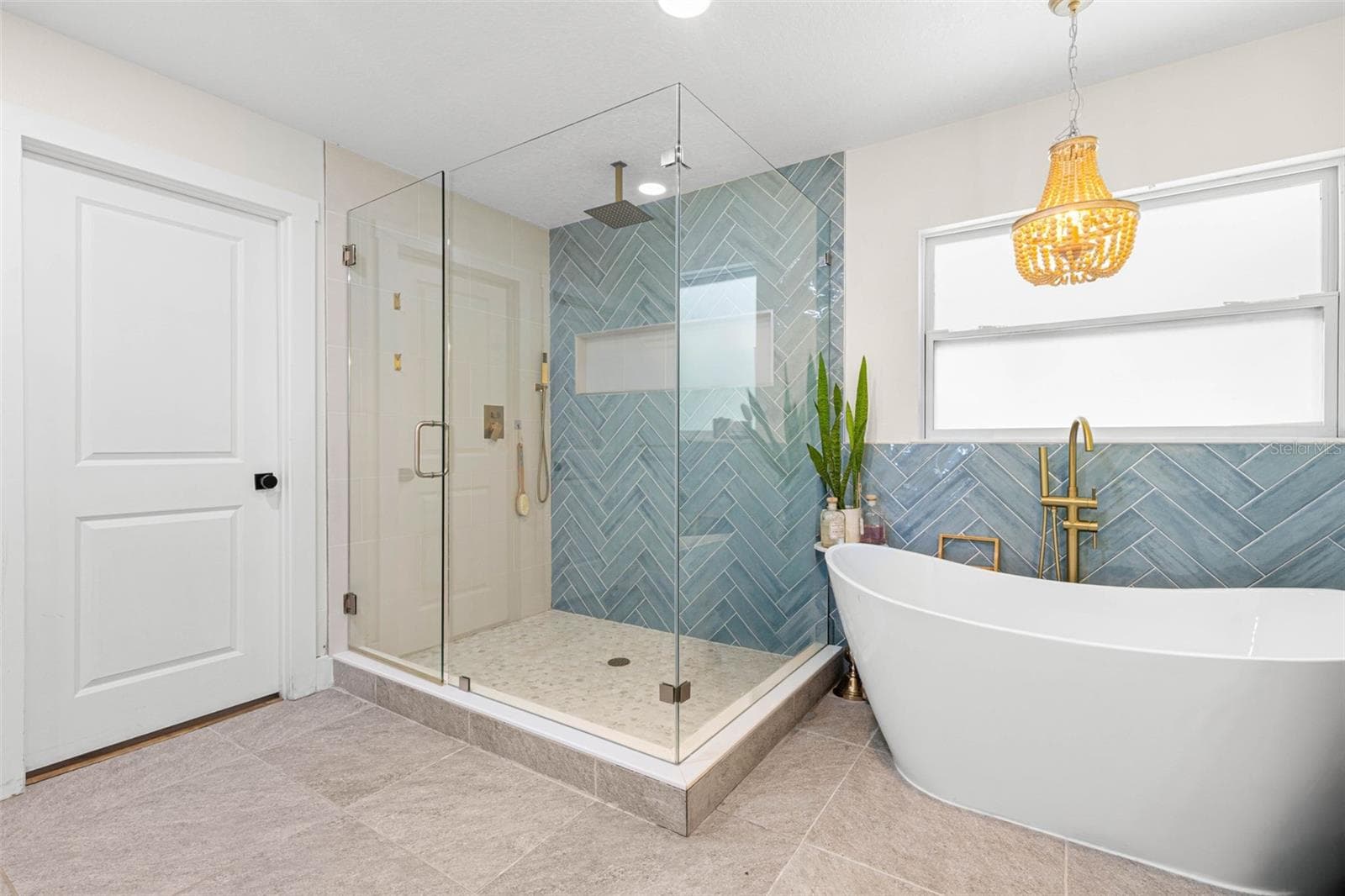A freestanding soaking tub takes center stage beneath an elegant gold chandelier, complemented by a floor-mounted gold tub filler and beautiful blue-green herringbone tile. The adjoining glass-enclosed shower completes this luxurious, spa-inspired retreat. - 3013 GRAHAM LN, TAMPA