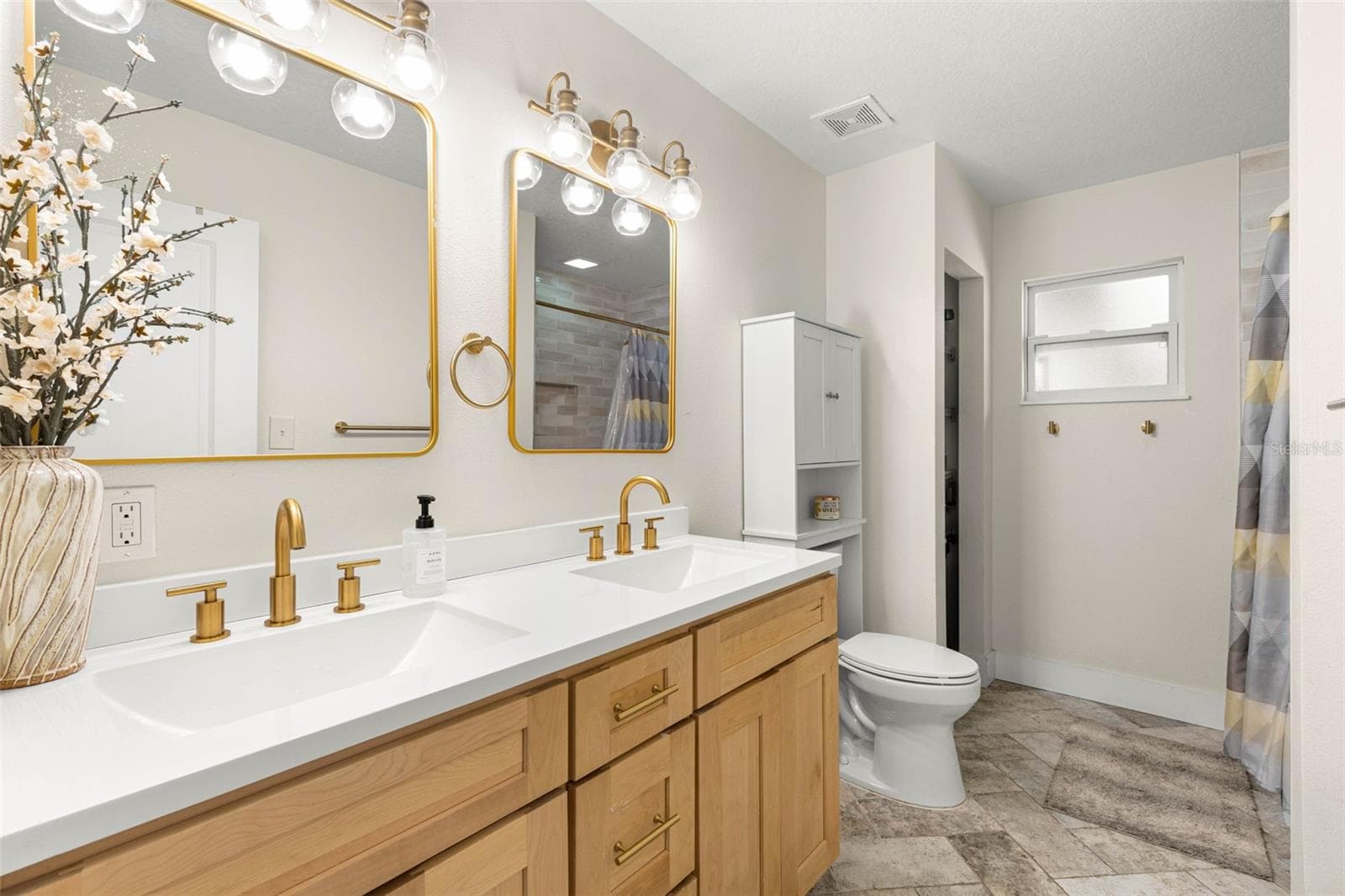 The stylish second bathroom features a double-sink vanity with natural wood cabinetry, crisp white countertops, brushed gold fixtures, coordinating mirrors, and contemporary glass-globe lighting. Neutral tile flooring and a tub/shower combination complete this thoughtfully updated space. - 3013 GRAHAM LN, TAMPA