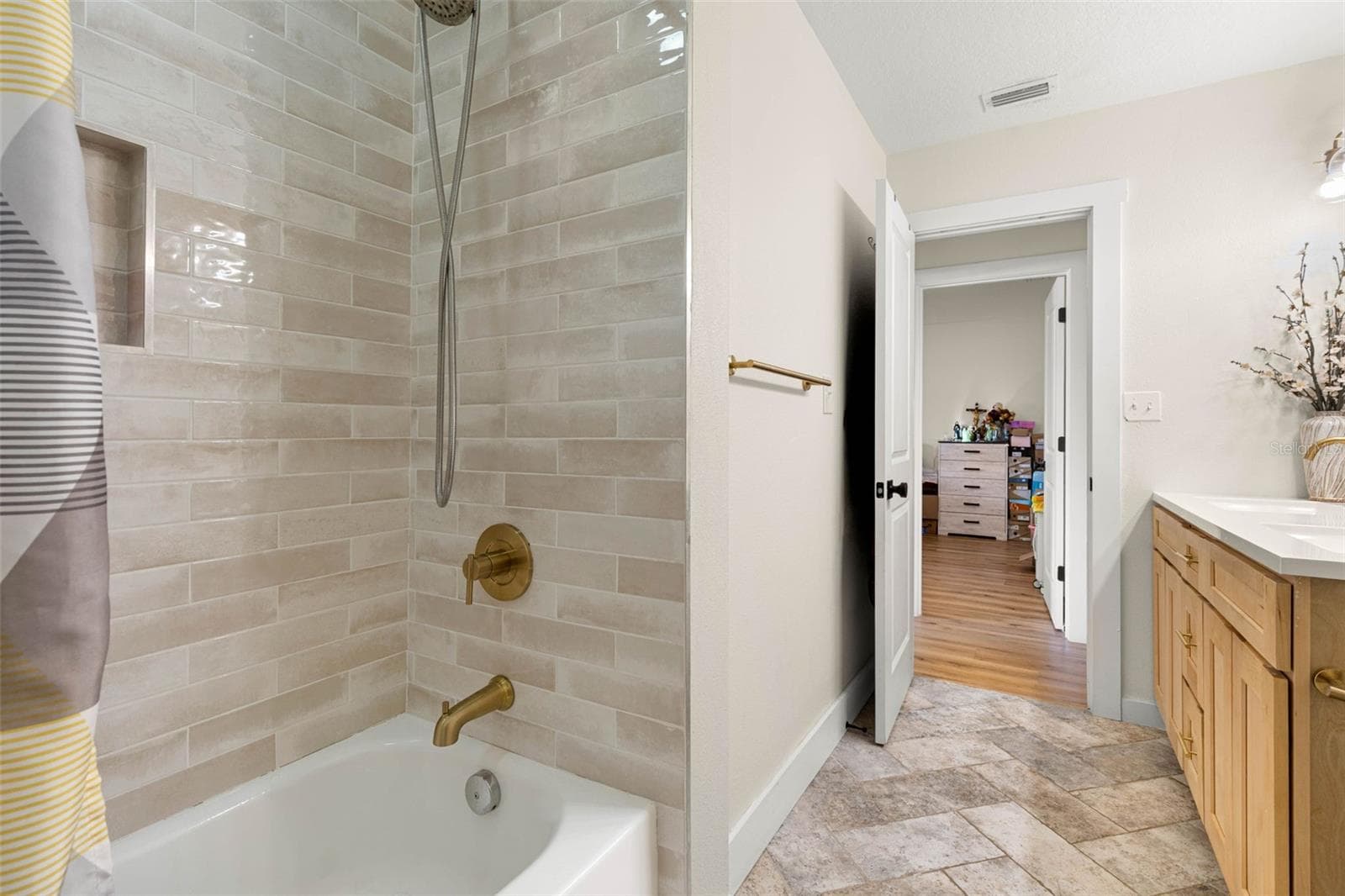 The second bathroom's tub/shower combination features glossy, neutral-toned subway tile, a recessed storage niche, and brushed gold fixtures, including a convenient handheld showerhead. Coordinating tile flooring and warm wood cabinetry complete the updated space. - 3013 GRAHAM LN, TAMPA