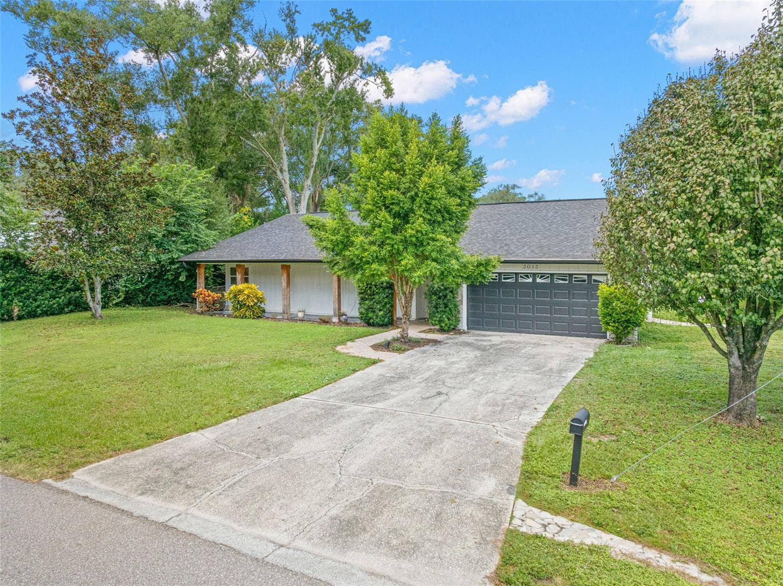 A wide concrete driveway leads to the attached two-car garage, offering convenient parking and additional storage. Mature shade trees, lush greenery, and an expansive front lawn enhance the home's curb appeal. - 3013 GRAHAM LN, TAMPA