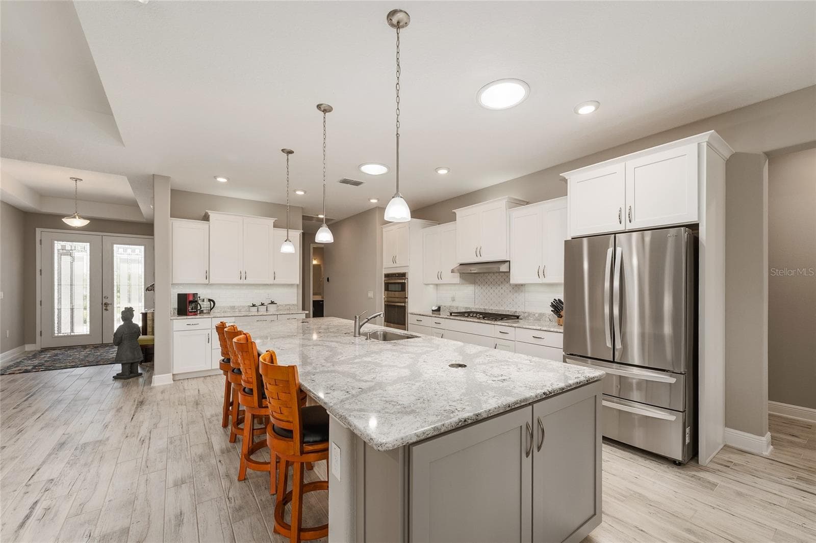 Beautifully appointed kitchen featuring staggered cabinetry, convenient pull-out drawers, a neutral tile backsplash, and two solar tubes that fill the space with natural light. GE gas range, GE dishwasher, and LG refrigerator complement the impressive 12' x 4.5' Cambria quartz island, complete with pop-up outlets and abundant additional storage. - 8290 SW 92ND CIR, OCALA