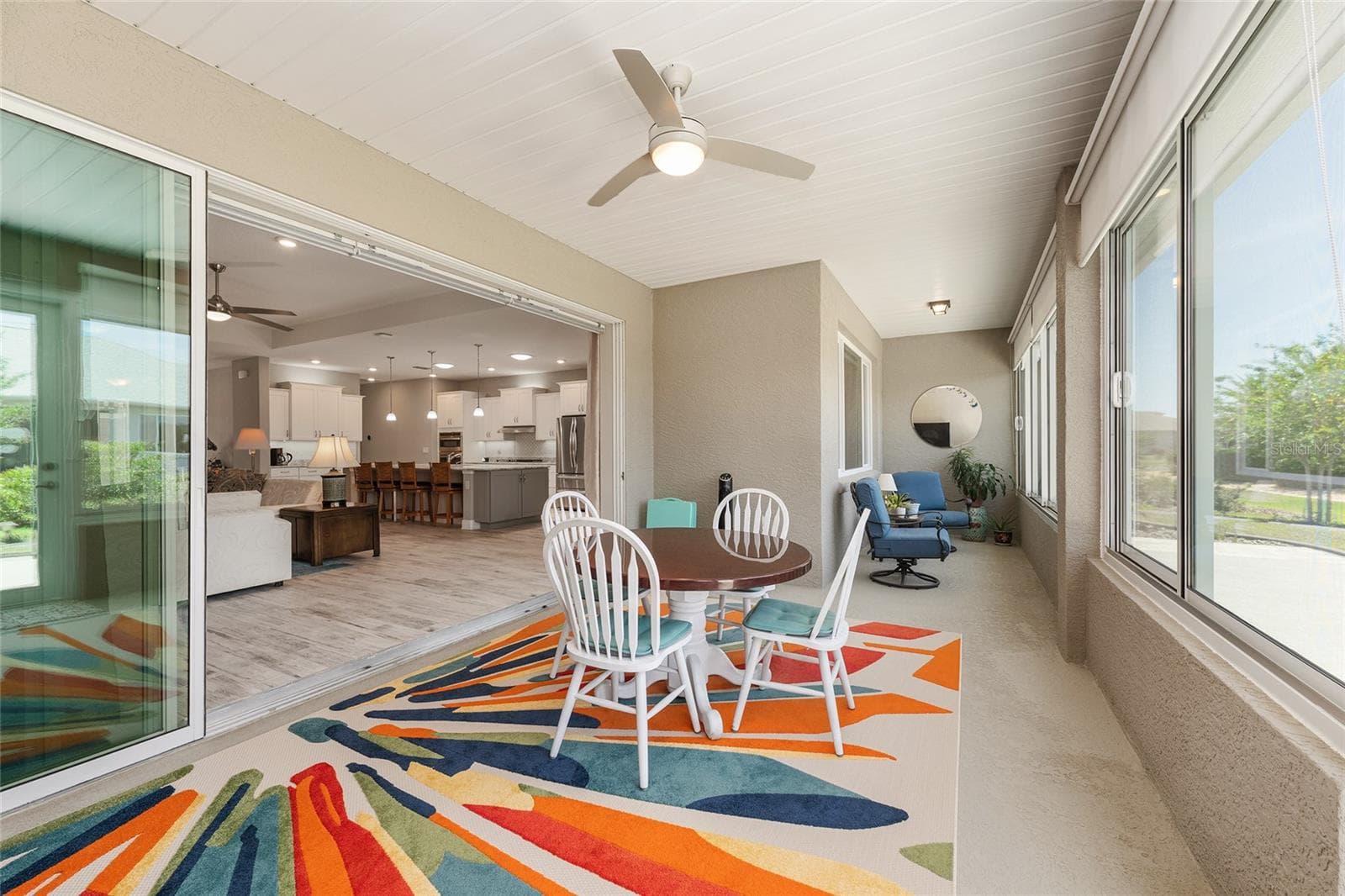 Inviting enclosed lanai featuring a seamless, zero-entry transition from the great room, finished walls, a 24-inch knee wall, ceiling fan with integrated lighting, convenient GFCI outlet, and custom solar shades for added comfort and privacy. - 8290 SW 92ND CIR, OCALA