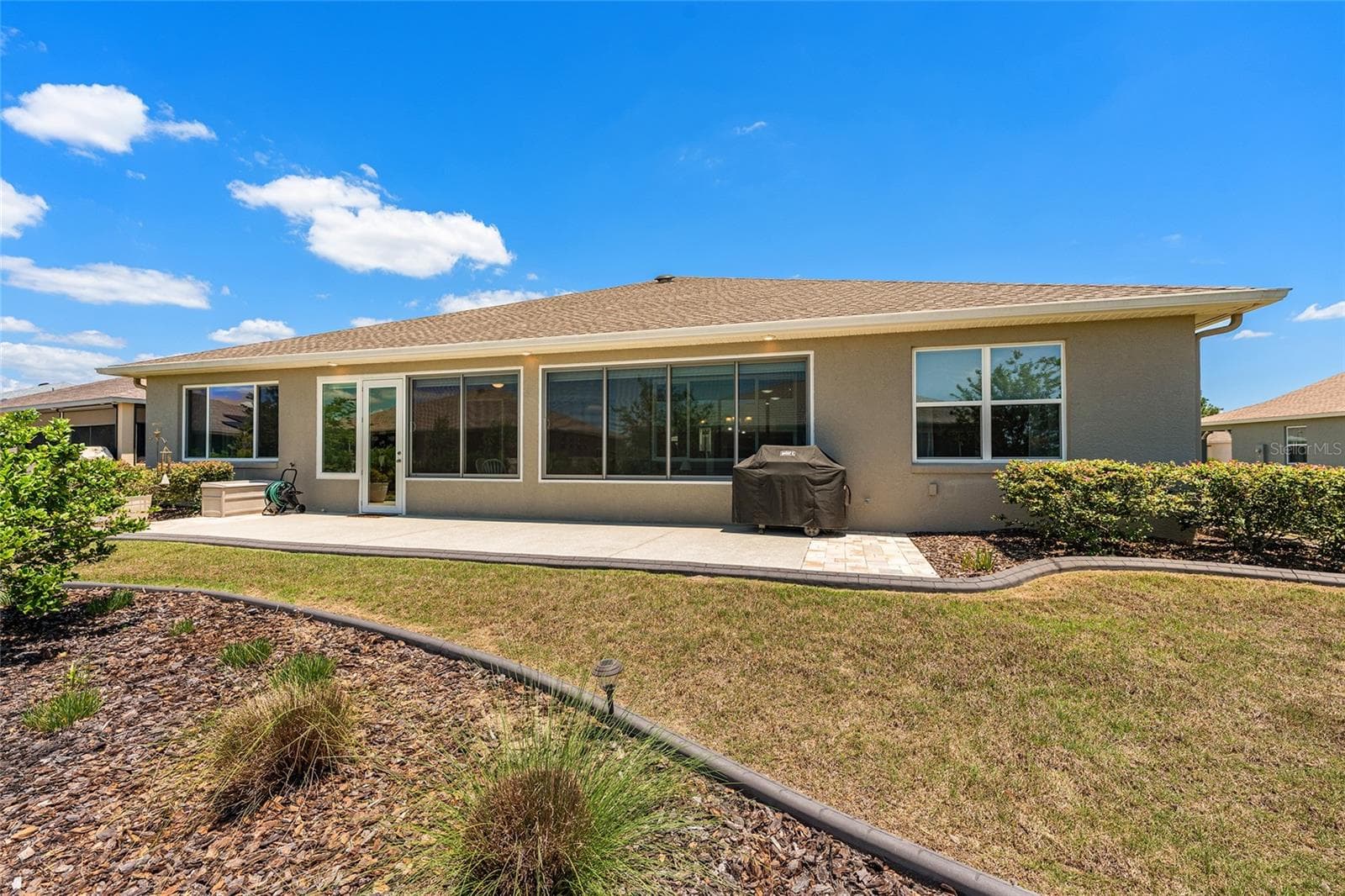 Beautifully landscaped backyard featuring a spacious 38' x 10' patio, soffit lighting, and a dedicated gas line for the included barbecue grill. An ideal setting for outdoor entertaining and relaxation. - 8290 SW 92ND CIR, OCALA