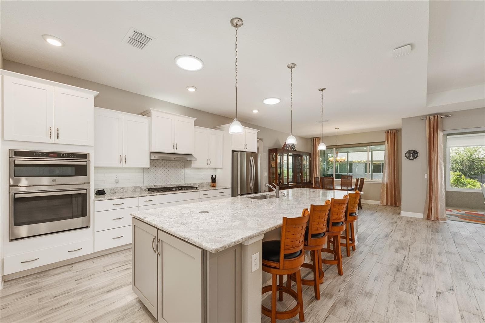Beautifully appointed kitchen featuring an expansive Cambria quartz island with seating, staggered cabinetry, stainless steel appliances, GE double convection ovens with microwave, and two solar tubes that fill the space with natural light. - 8290 SW 92ND CIR, OCALA