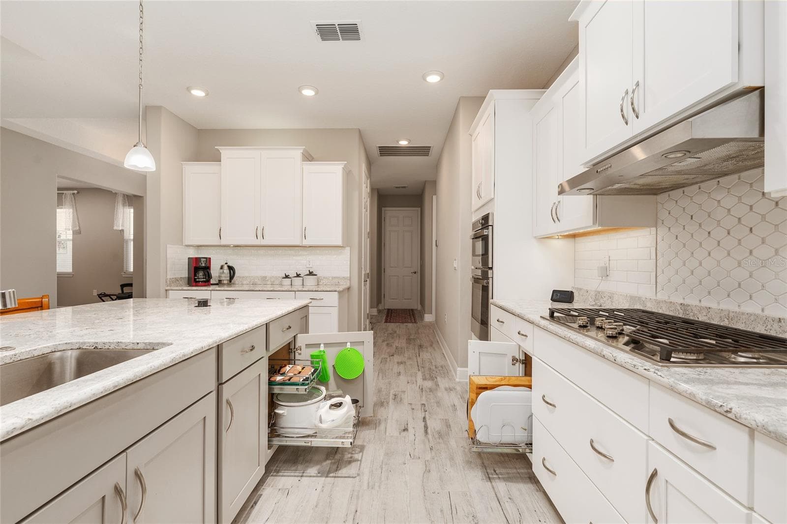Thoughtfully designed kitchen featuring a large single-basin sink with built-in soap dispenser, convenient pull-out storage organizers, Cambria quartz countertops, and a decorative tile backsplash—combining functionality with everyday convenience. - 8290 SW 92ND CIR, OCALA