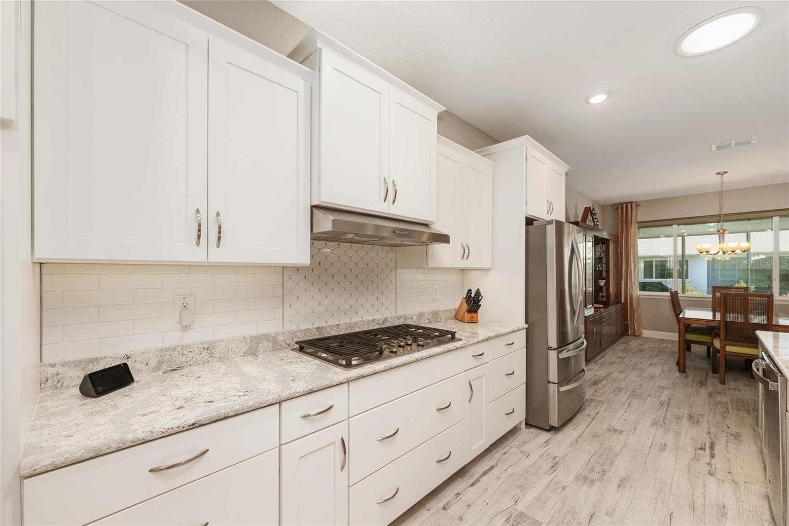 Well-appointed kitchen featuring abundant pot drawers, stainless steel appliances, a GE five-burner gas cooktop, neutral tile backsplash, Cambria quartz countertops, and an open flow into the dining area. - 8290 SW 92ND CIR, OCALA