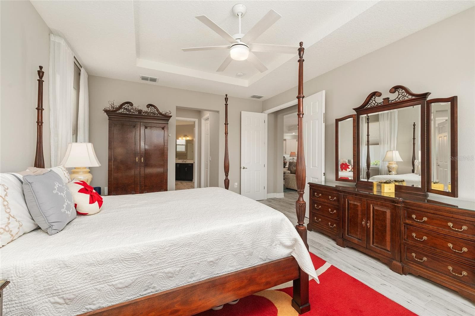Another view of the first primary suite, currently used as the owner's suite, featuring a double-door entry, tray ceiling, ceramic plank flooring, and convenient access to the ensuite bathroom. - 8290 SW 92ND CIR, OCALA
