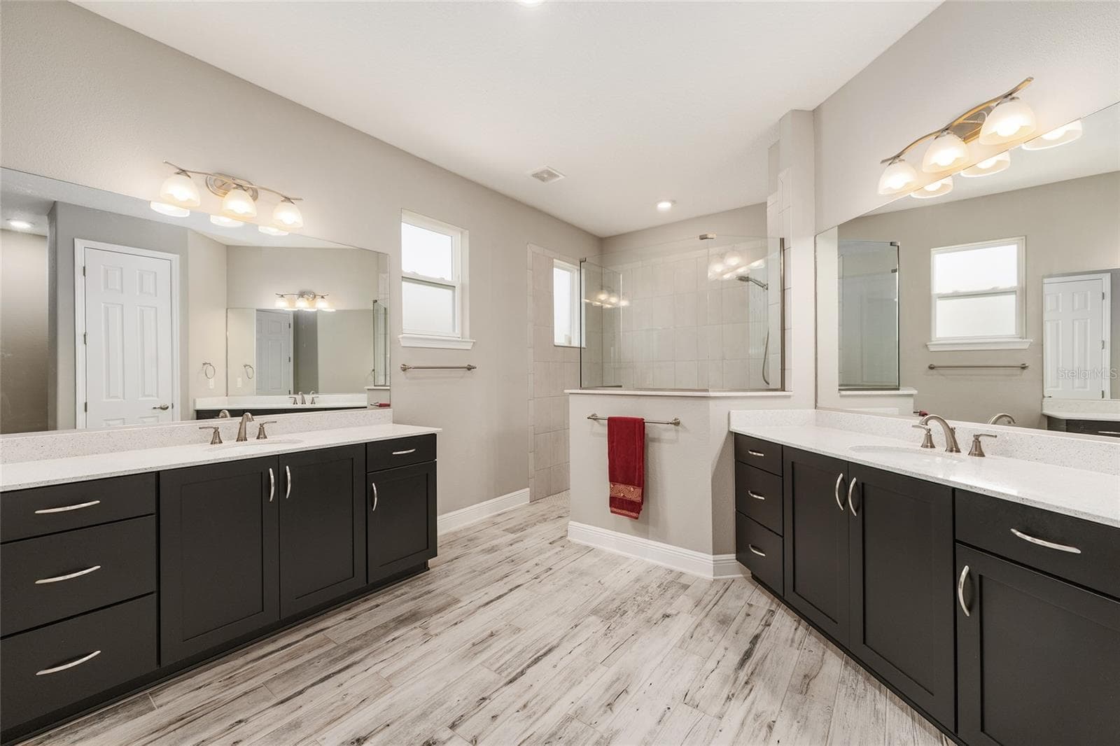 Spacious first primary ensuite bathroom featuring separate vanities with generous countertop space, abundant cabinet and drawer storage, ceramic plank flooring, and a large walk-in shower with glass enclosure. - 8290 SW 92ND CIR, OCALA