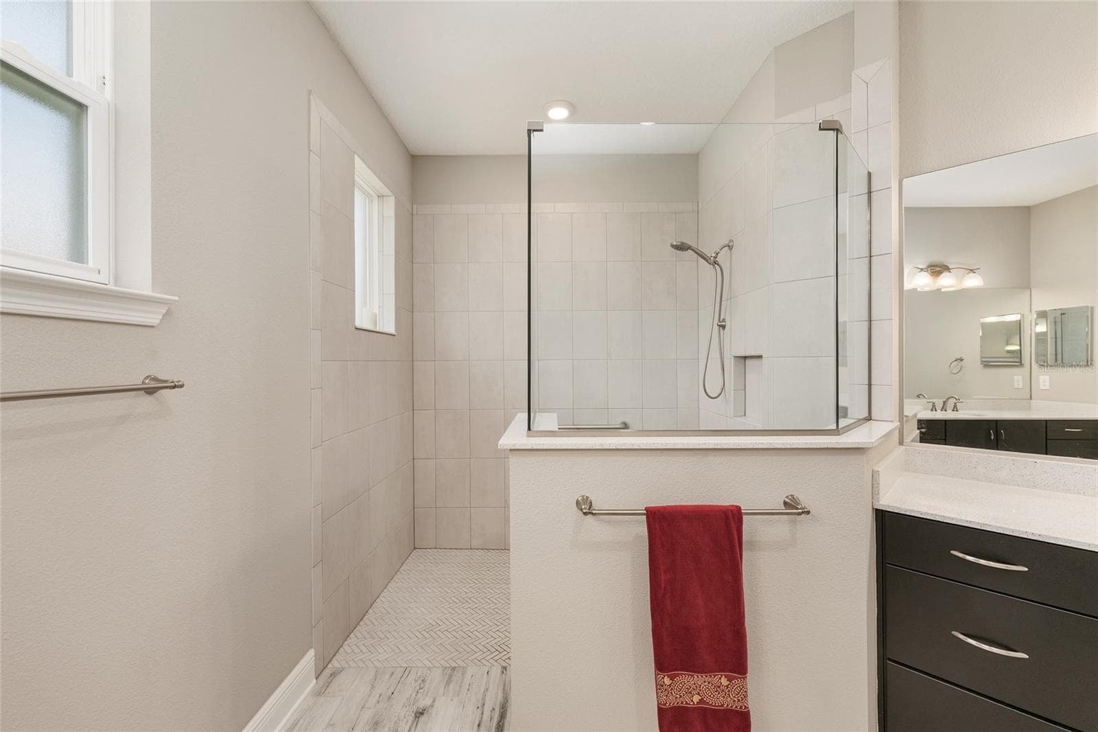 Spacious first primary ensuite bathroom featuring a large zero-entry walk-in shower with glass enclosure, tile surround, built-in niche, handheld shower fixture, and a bright, open design for everyday comfort and convenience. - 8290 SW 92ND CIR, OCALA
