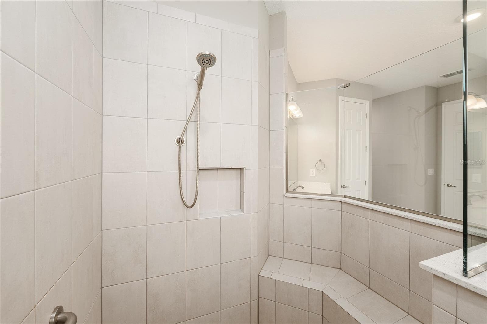 Closer view of the first primary suite's beautifully tiled shower, showcasing the integrated corner bench and thoughtfully designed space for added comfort and convenience. - 8290 SW 92ND CIR, OCALA