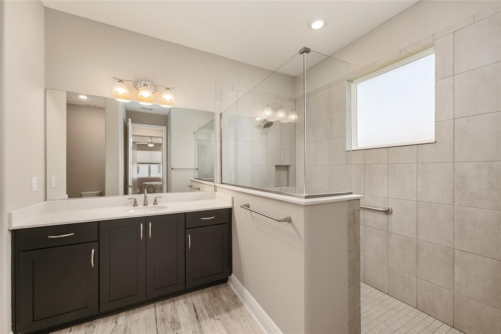 Second primary ensuite bathroom showcasing a spacious zero-entry walk-in shower with a glass enclosure, tiled walls, built-in niche, and natural light from the privacy window. - 8290 SW 92ND CIR, OCALA