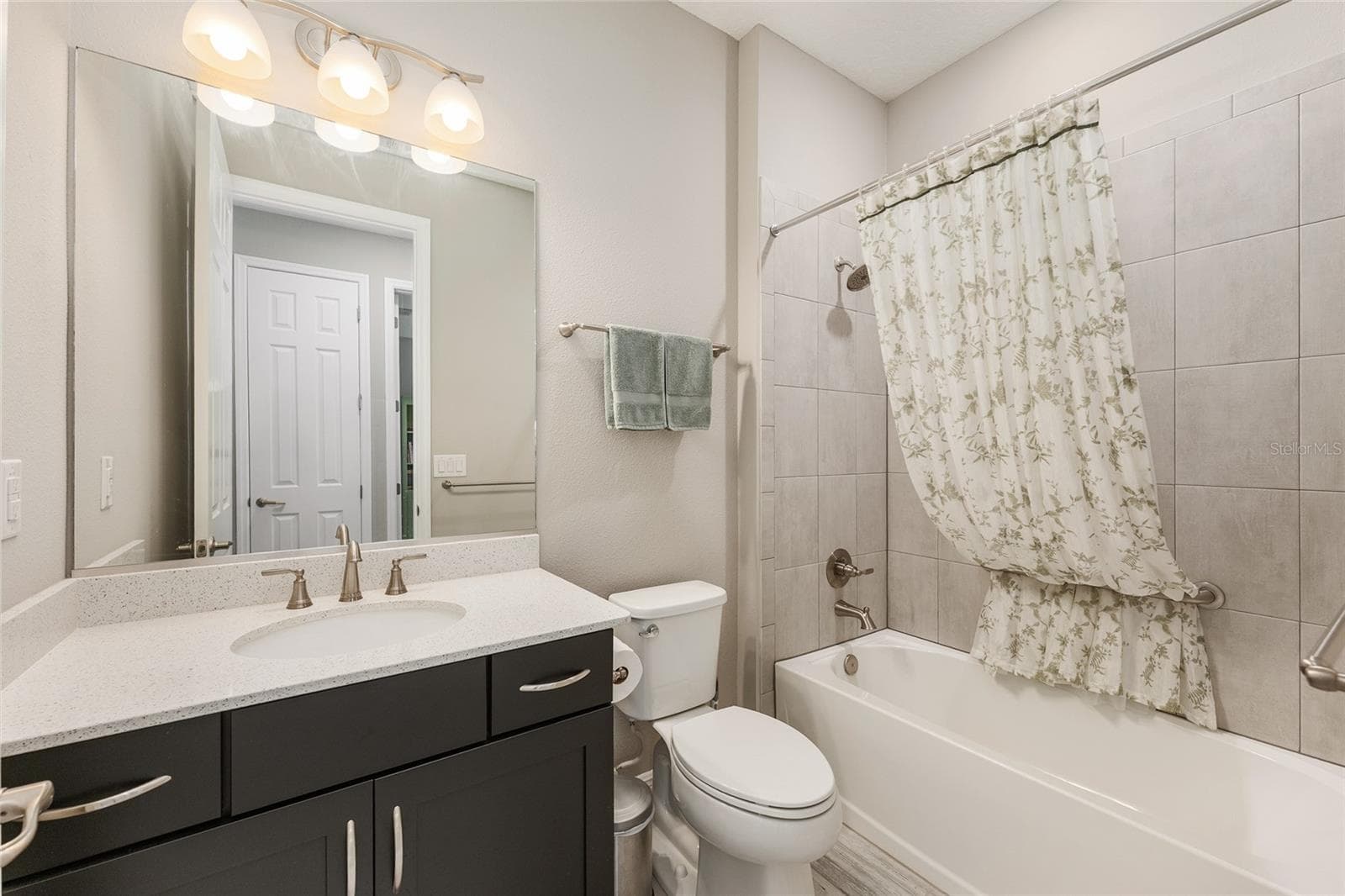 Conveniently located near the third bedroom, this guest bathroom features a spacious vanity with contrasting dark cabinetry, a large mirror, and a tiled tub/shower combination. - 8290 SW 92ND CIR, OCALA