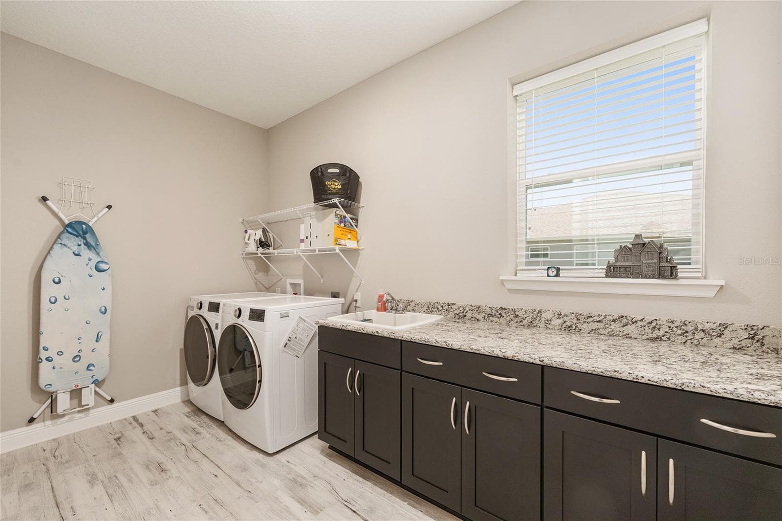 Spacious laundry room featuring abundant cabinetry, expansive granite countertops, a convenient utility sink, and a window providing natural light. Includes an LG front-load washer and gas dryer, with an additional electric dryer connection for flexibility. - 8290 SW 92ND CIR, OCALA