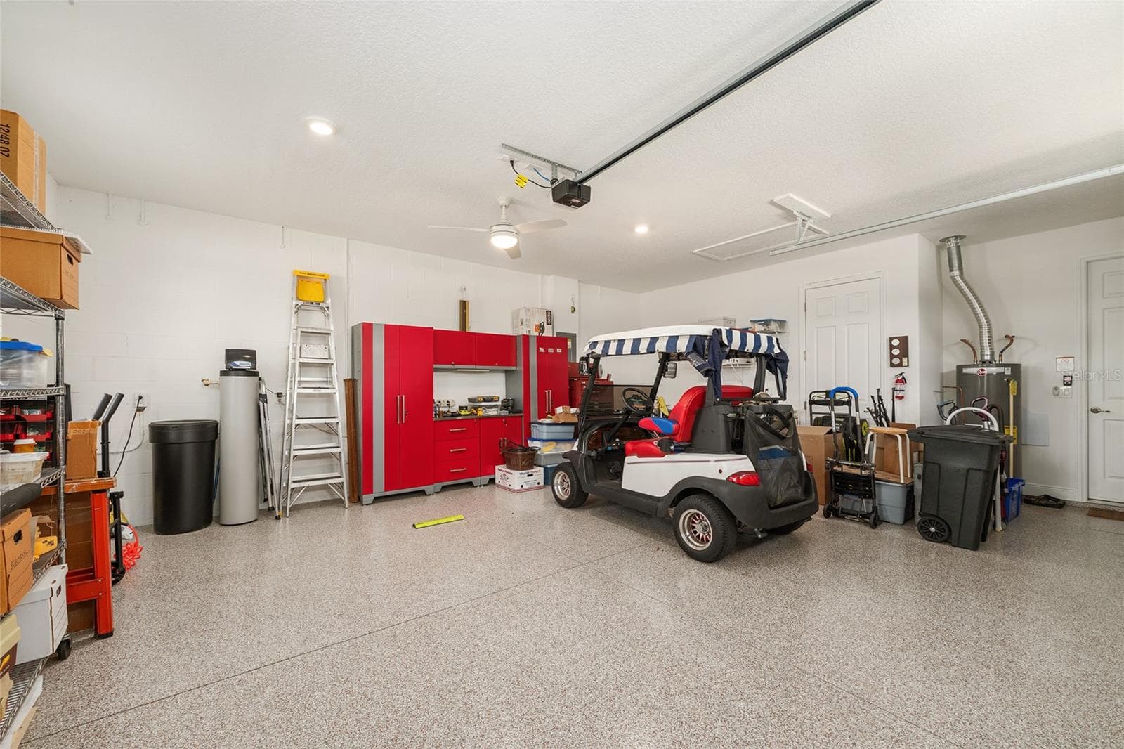 Spacious two-car garage featuring durable epoxy flooring, an insulated garage door with heavy-duty springs, recessed lighting, a ceiling fan with integrated lighting, a convenient utility sink, and additional electrical outlets throughout. Plenty of room for parking, storage, and projects. - 8290 SW 92ND CIR, OCALA