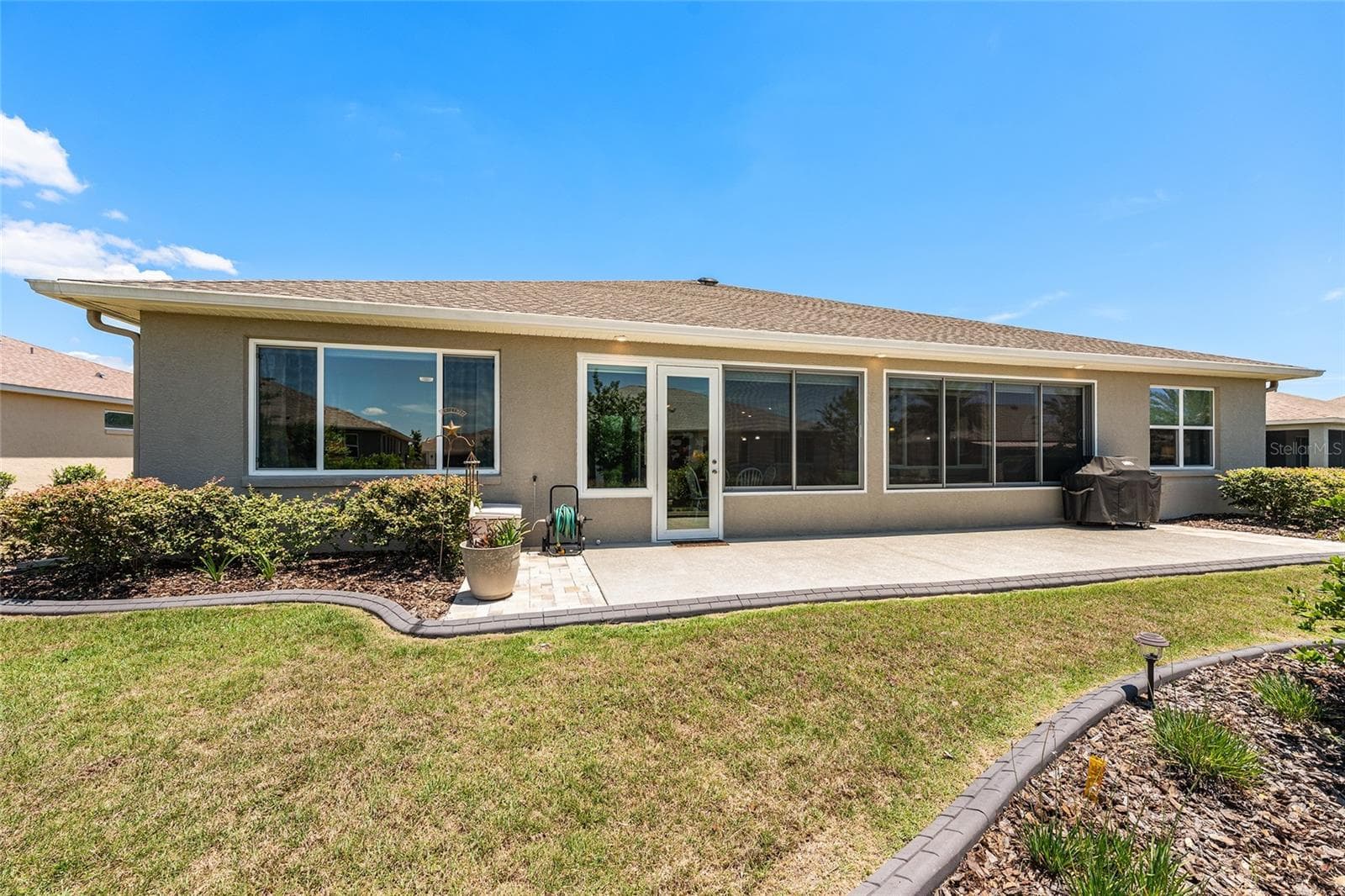 Full rear elevation showcasing the home's attractive architectural design, expansive windows, and generous outdoor living space. The extended patio and landscaped surroundings complement the home's spacious backyard setting. - 8290 SW 92ND CIR, OCALA