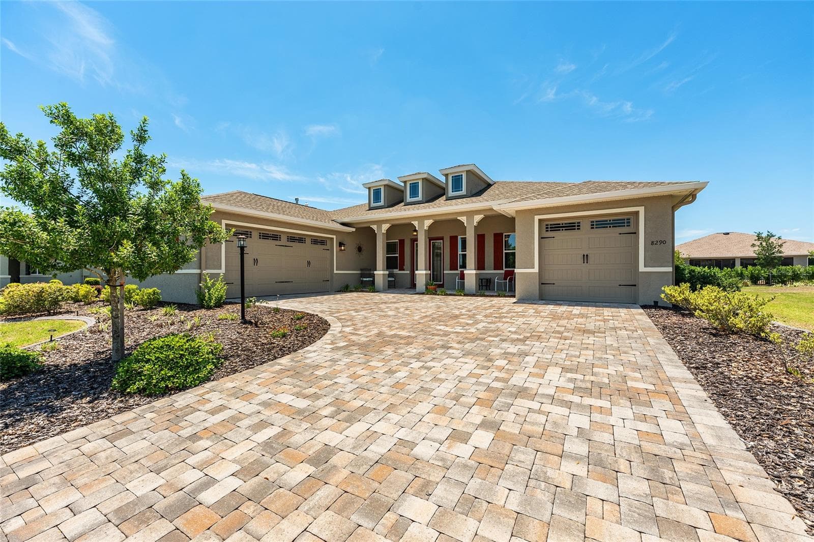 Beautiful 2021 Aberdeen model in West Kestrel at Candler Hills, showcasing exceptional curb appeal with an expansive paver driveway, inviting covered front porch, distinctive architectural details, and a desirable split three-car garage. Professionally landscaped grounds feature Zoysia grass, decorative concrete curbing, full-yard irrigation with Hunter Hydrawise controls, and gutters with downspouts. - 8290 SW 92ND CIR, OCALA