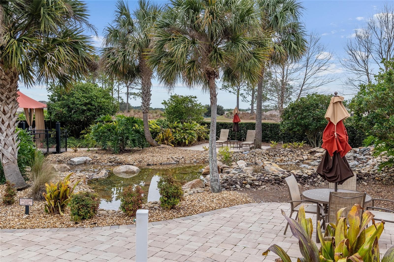 Tranquil water feature at The Lodge at Candler Hills, surrounded by lush tropical landscaping, natural stone accents, and inviting outdoor seating areas—creating a peaceful retreat to relax and enjoy the beautiful surroundings. - 8290 SW 92ND CIR, OCALA