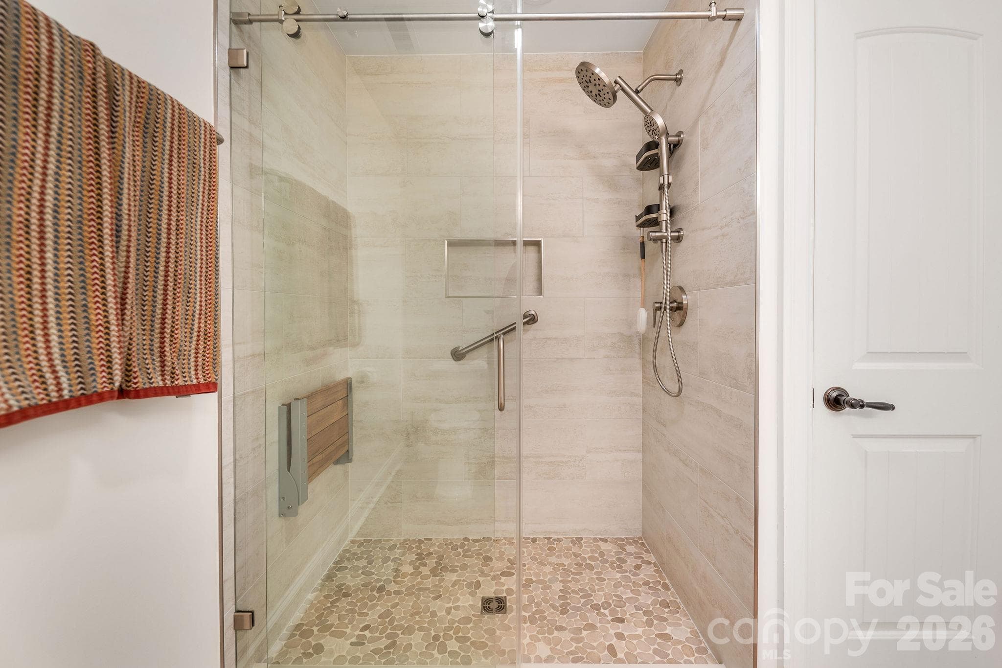 Spacious walk-in shower featuring frameless glass, custom tile, and built-in seating - 28 Penley Park Drive, Weaverville