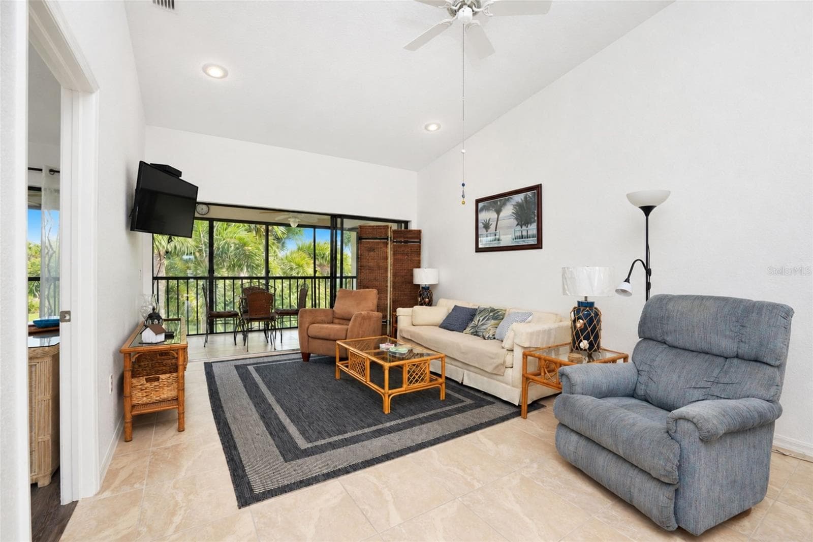 The living room has a cathedral ceiling, ceiling fan, tiled flooring and sliding glass doors to the lanai. - 4260 PLACIDA RD #9C, ENGLEWOOD