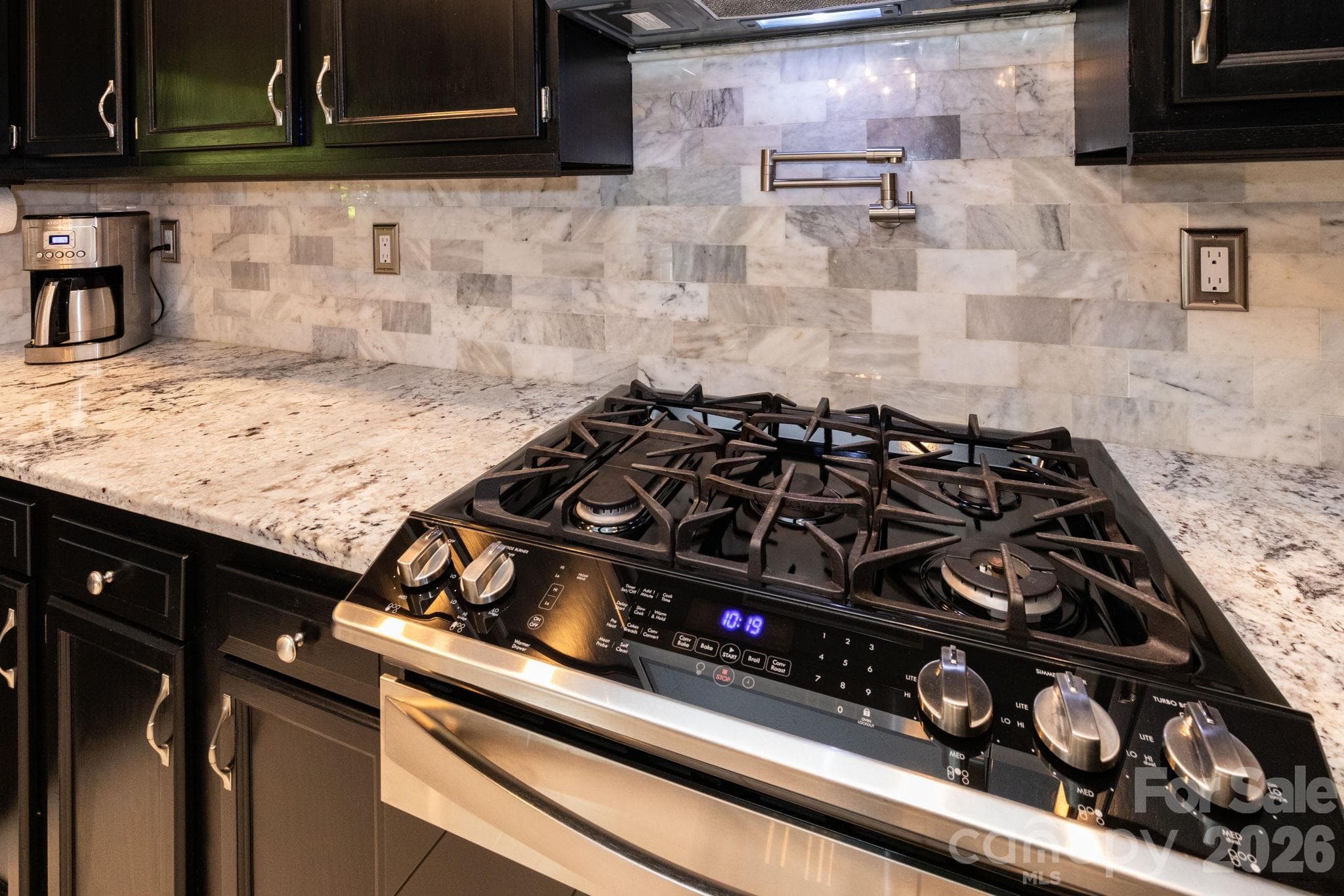 Kitchen detail showcasing the gas range, pot-filler faucet, tile backsplash, and surrounding counter space. - 139 Lone Eagle Lane, Hendersonville