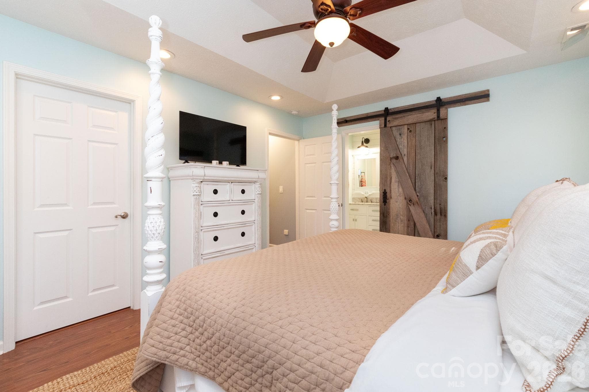 Primary bedroom view highlighting the tray ceiling, wood flooring, and rustic sliding barn door. - 139 Lone Eagle Lane, Hendersonville