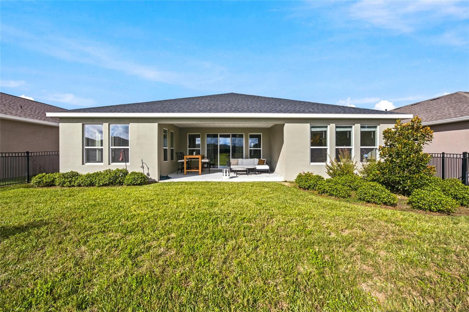 Rear exterior showcasing the covered patio, landscaped yard and black metal fencing. - 4497 NW 54TH TER, OCALA