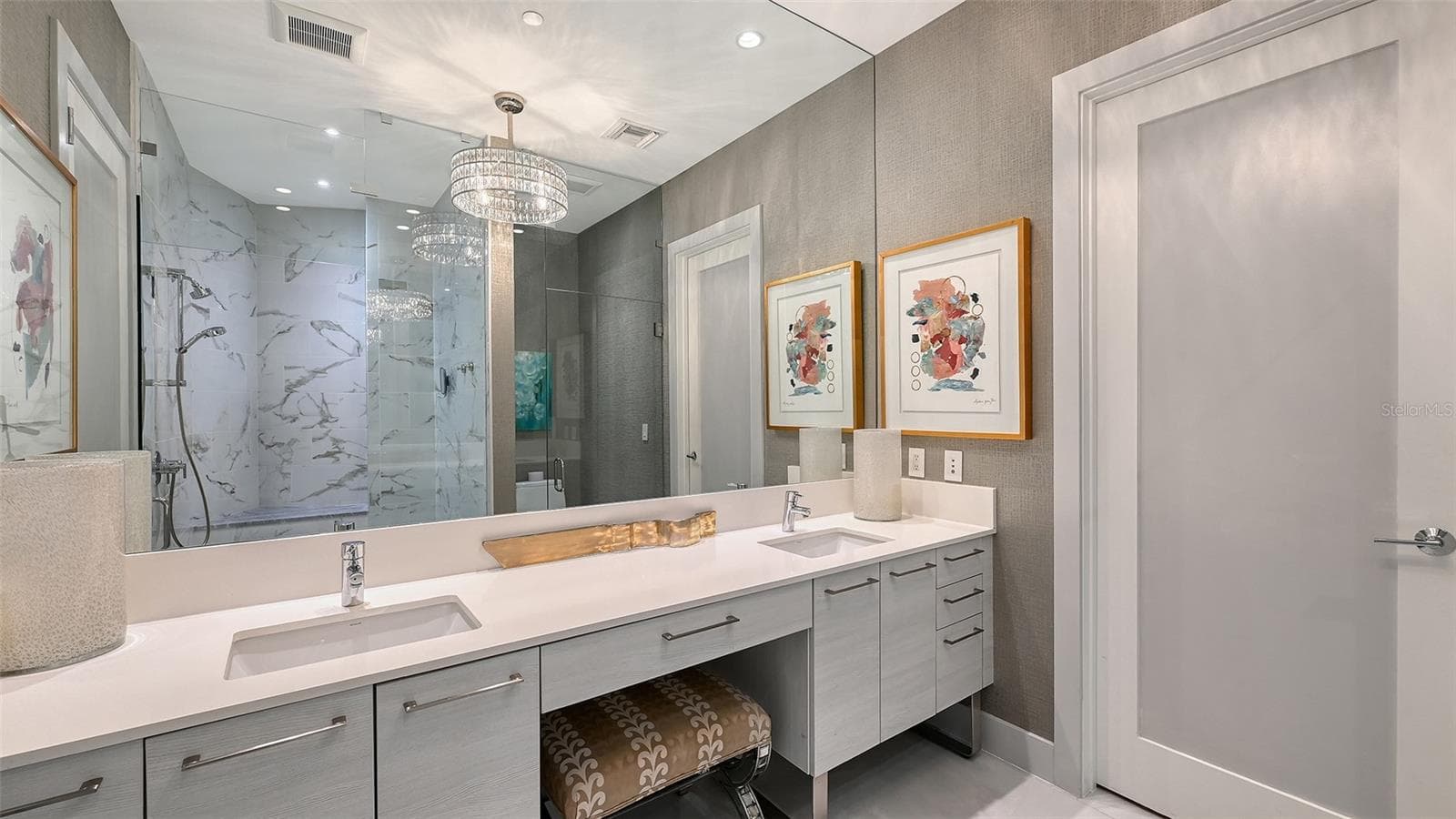 An elegant primary bath featuring dual sinks, a dedicated makeup vanity with an oversized mirror, and a custom chandelier for a touch of refined luxury. - 1155 N GULFSTREAM AVE #207, SARASOTA