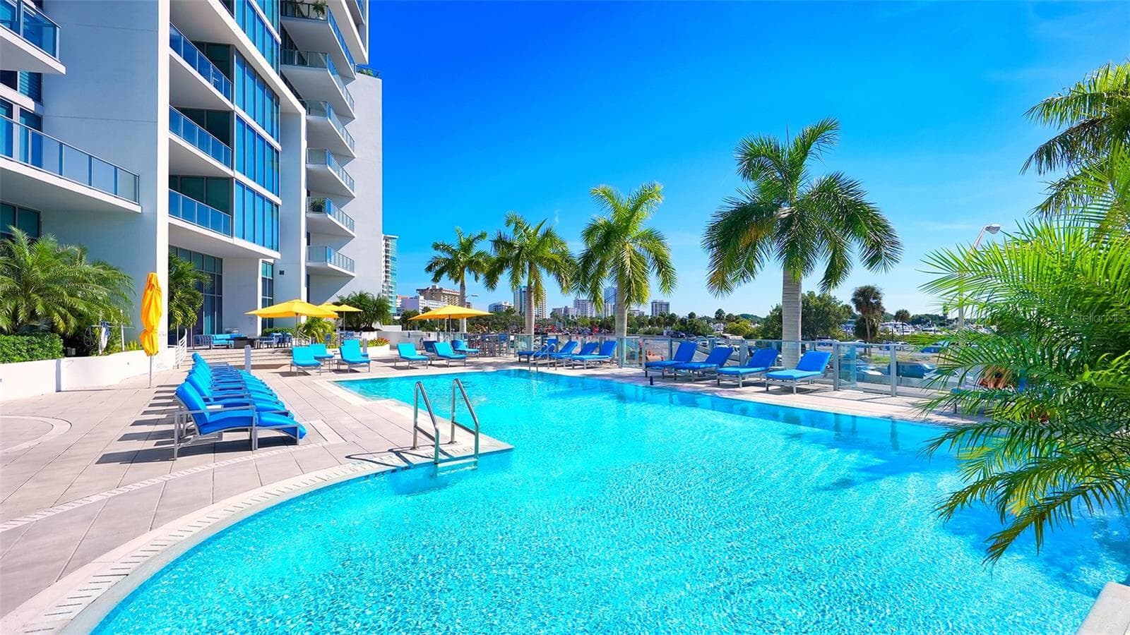 A sparkling blue resort-style pool surrounded by an elegant sun deck with inviting lounge chairs and umbrellas, creating the perfect setting for relaxation and soaking up the Florida sunshine. - 1155 N GULFSTREAM AVE #207, SARASOTA