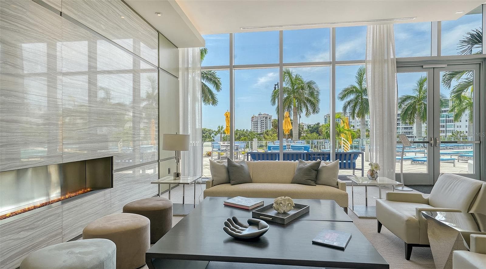 An elegant lobby seating area framed by floor-to-ceiling windows overlooking the resort-style pool, offering a bright, inviting space to relax and enjoy the view. - 1155 N GULFSTREAM AVE #207, SARASOTA