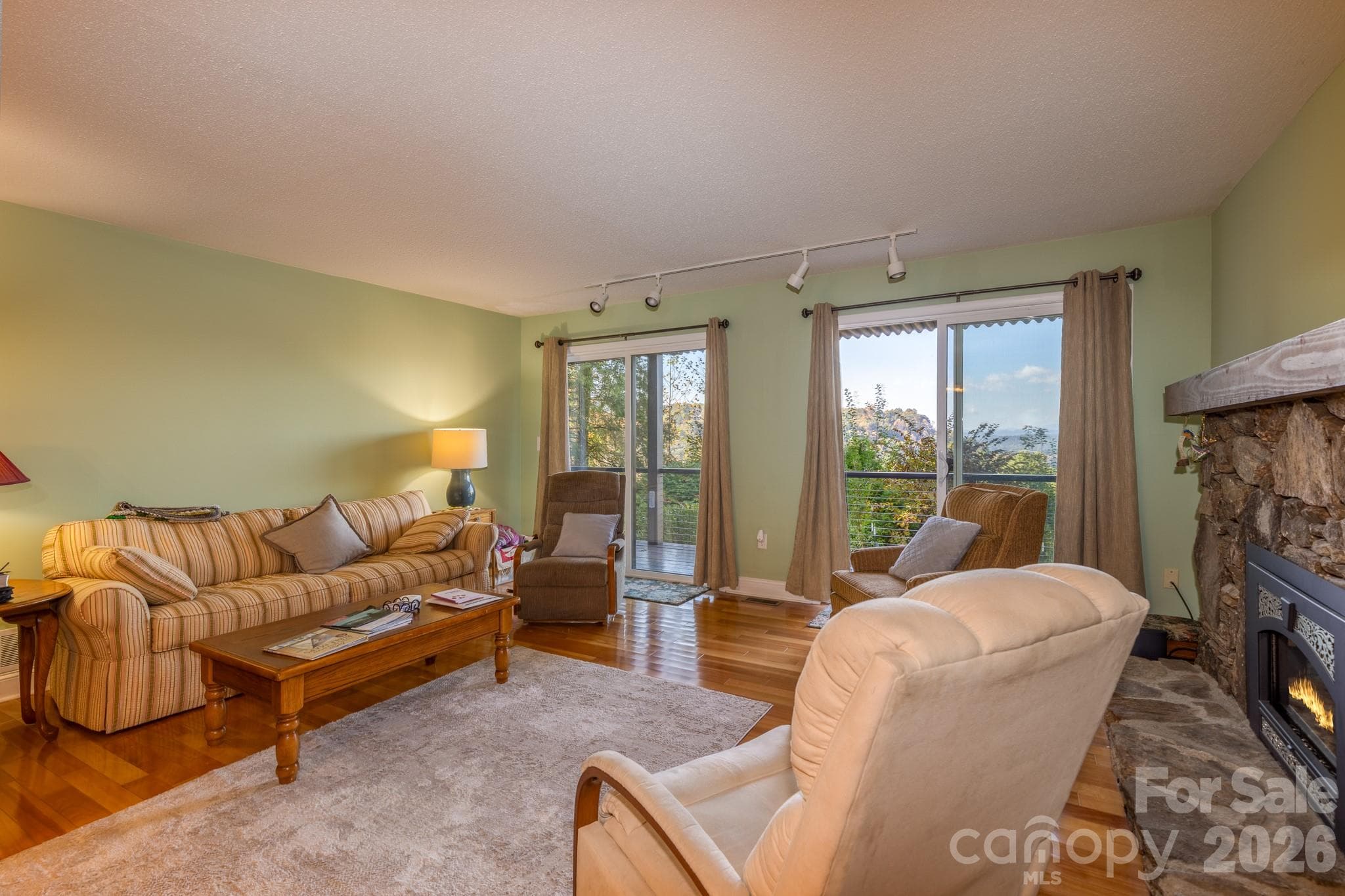 Spacious living room featuring beautiful hardwood floors, a striking native stone fireplace with gas insert, and two sliding glass doors opening to the covered deck with scenic mountain views. - 524 Three Mile Knob Road, Pisgah Forest