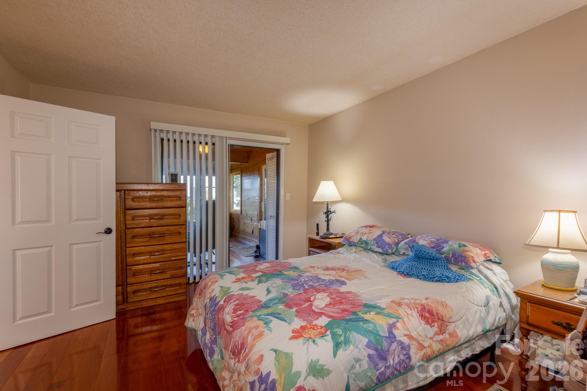 Another view of the primary bedroom highlighting beautiful hardwood floors and sliding glass doors leading into the wood-paneled sunroom. - 524 Three Mile Knob Road, Pisgah Forest