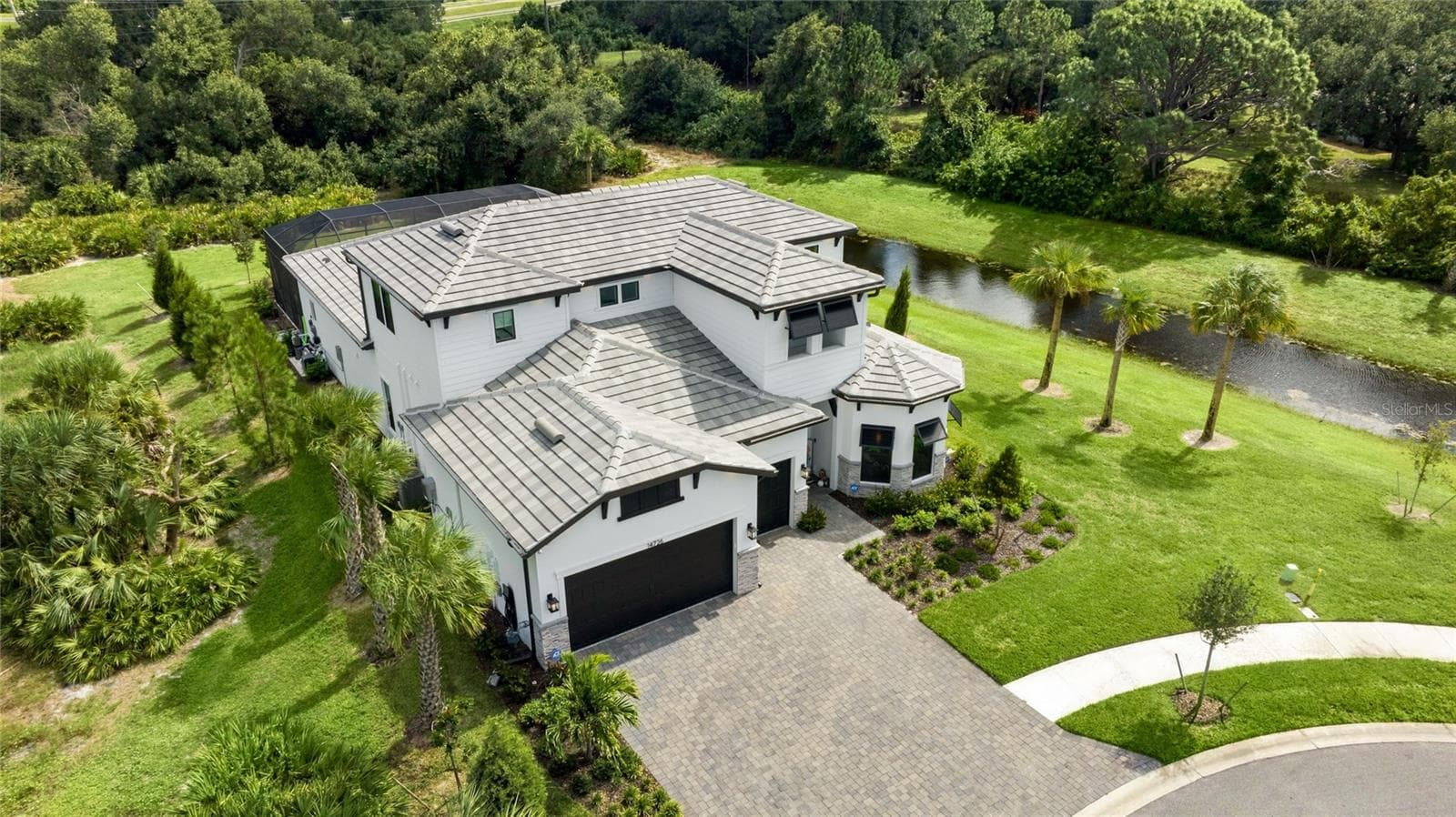 Elegant two-story residence featuring a striking modern coastal exterior, lush tropical landscaping, and an inviting paver driveway leading to a spacious three-car garage. - 14726 EAGLE BRANCH DR, NOKOMIS