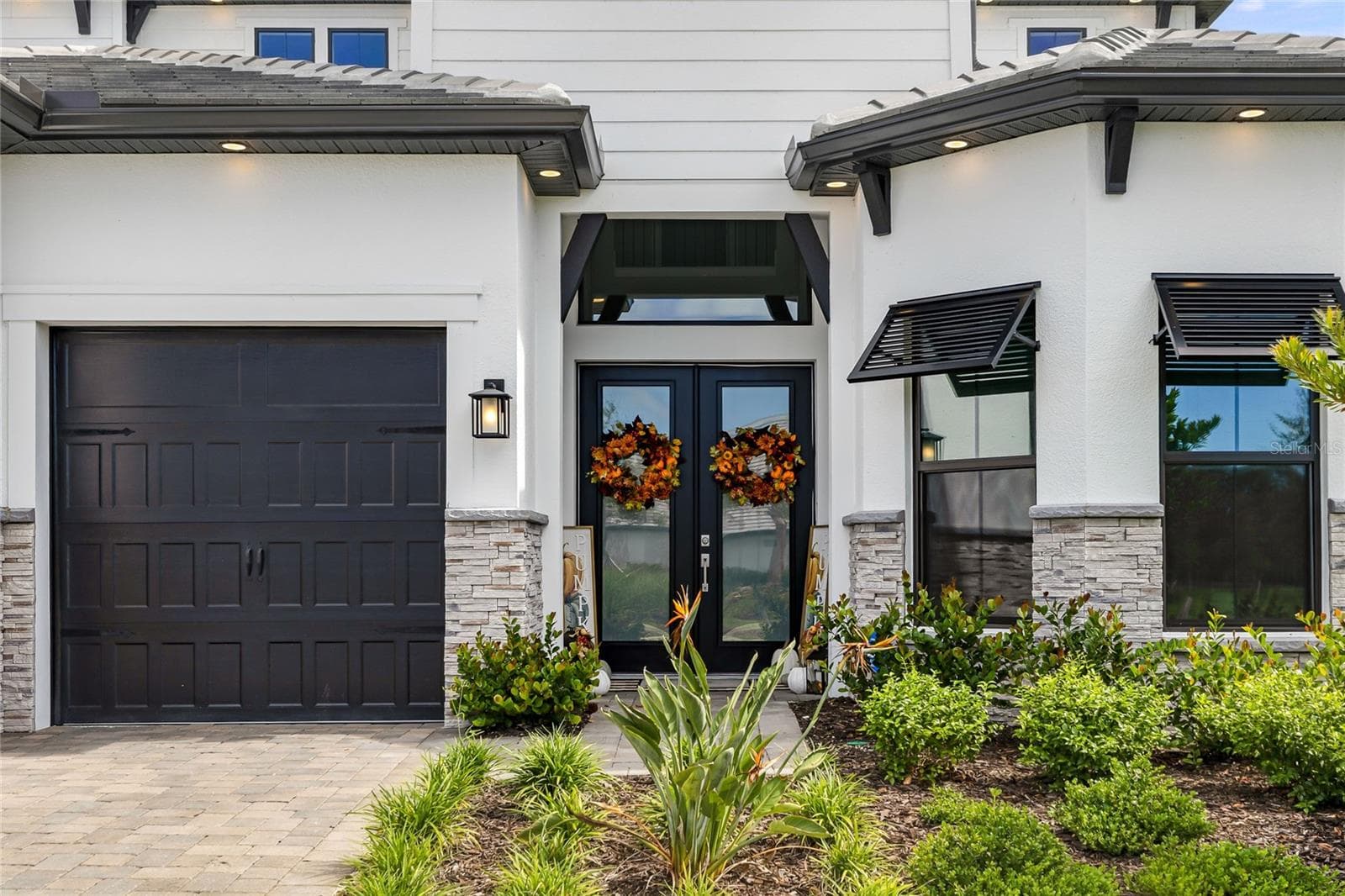 Elegant two-story residence featuring a striking modern coastal exterior, lush tropical landscaping, and an inviting paver driveway leading to a spacious three-car garage. - 14726 EAGLE BRANCH DR, NOKOMIS