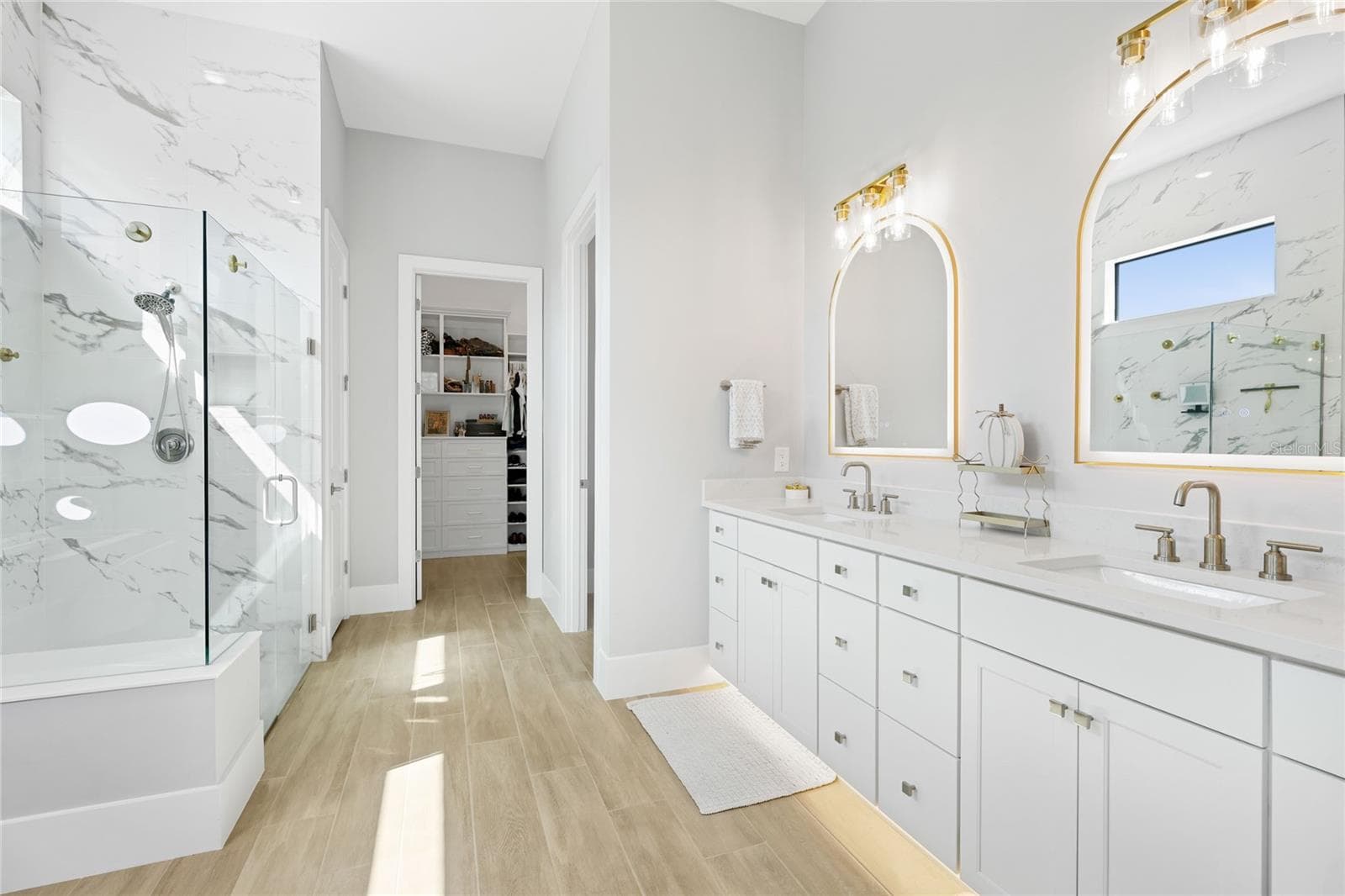 Primary Bathroom with walk in show with full glass enclosure, under lighting cabinetry, illuminating mirrors and expansive walk-in closet with custom shelving and cabinetry. - 14726 EAGLE BRANCH DR, NOKOMIS
