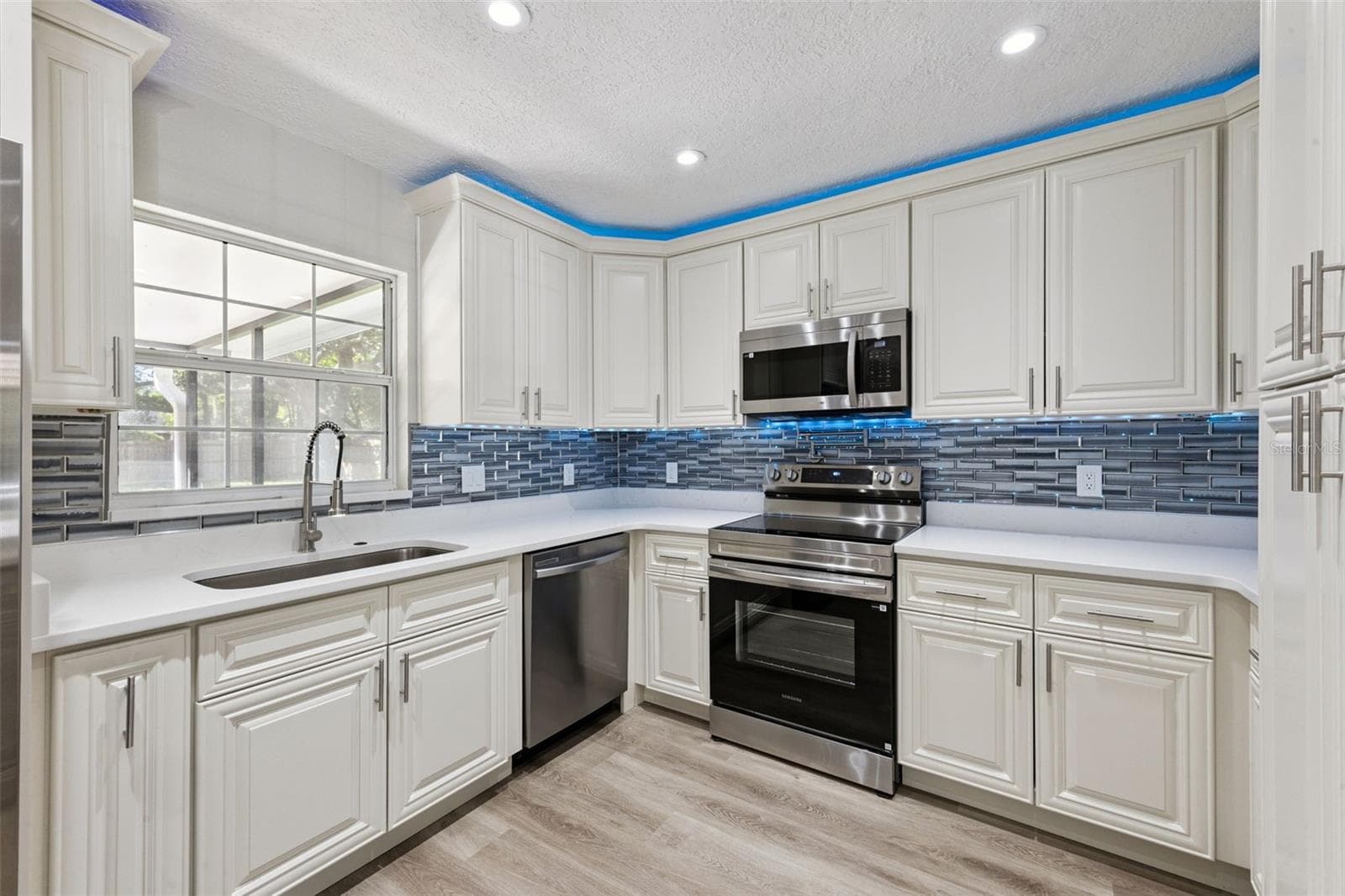 Kitchen Sink & Appliance Suite: Kitchen workspace featuring an undermount sink under a bright window, gooseneck faucet, stainless dishwasher, electric range, and blue LED accent lighting. - 720 GEORGIA AVE, LONGWOOD