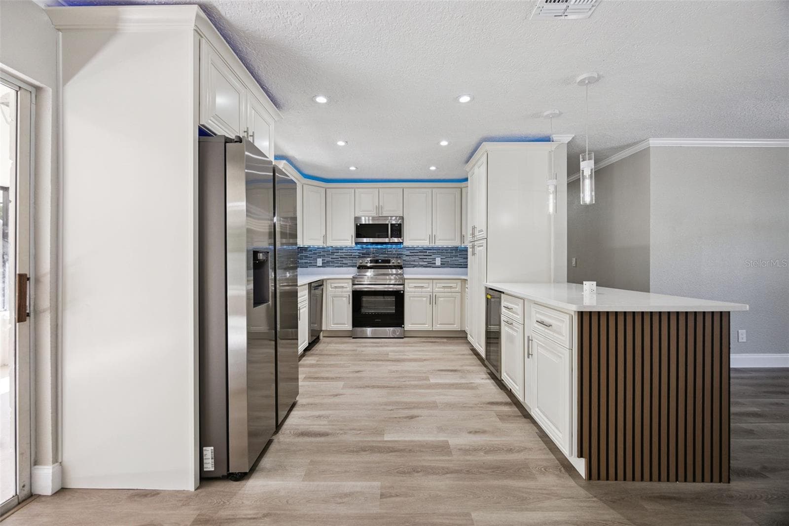 Refrigerator & Kitchen Suite: Full kitchen perspective highlighting the stainless steel French-door refrigerator, quartz counters, slatted island peninsula, and adjacent sliding patio door. - 720 GEORGIA AVE, LONGWOOD