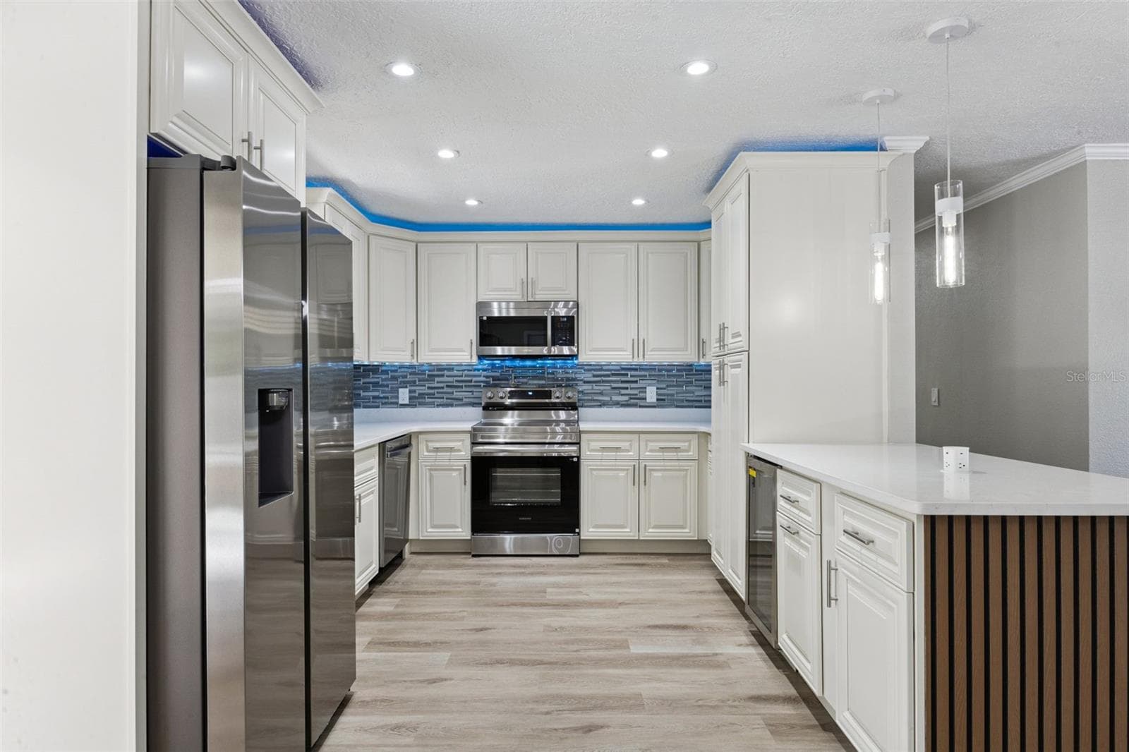 Complete Kitchen Layout: Centered view of the renovated kitchen showcasing seamless cabinetry, modern pendant fixtures, ambient ceiling LED lighting, and durable LVP flooring. - 720 GEORGIA AVE, LONGWOOD