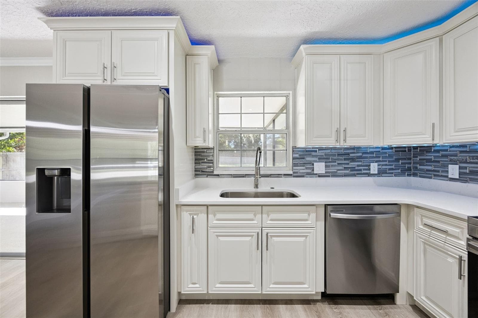 Kitchen Sink & Appliance Suite: Kitchen workspace featuring an undermount sink under a bright window, gooseneck faucet, stainless dishwasher, French-door refrigerator, and mosaic backsplash. - 720 GEORGIA AVE, LONGWOOD
