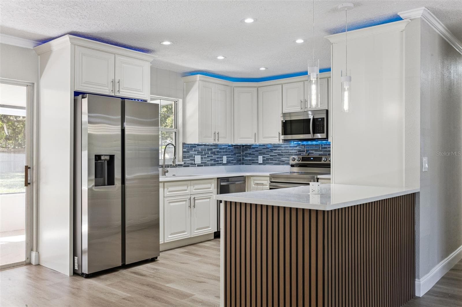Island Bar Accent Detail: Stylish kitchen peninsula showcasing modern vertical wood-slat accent paneling, quartz countertops, and a full stainless steel appliance package. - 720 GEORGIA AVE, LONGWOOD