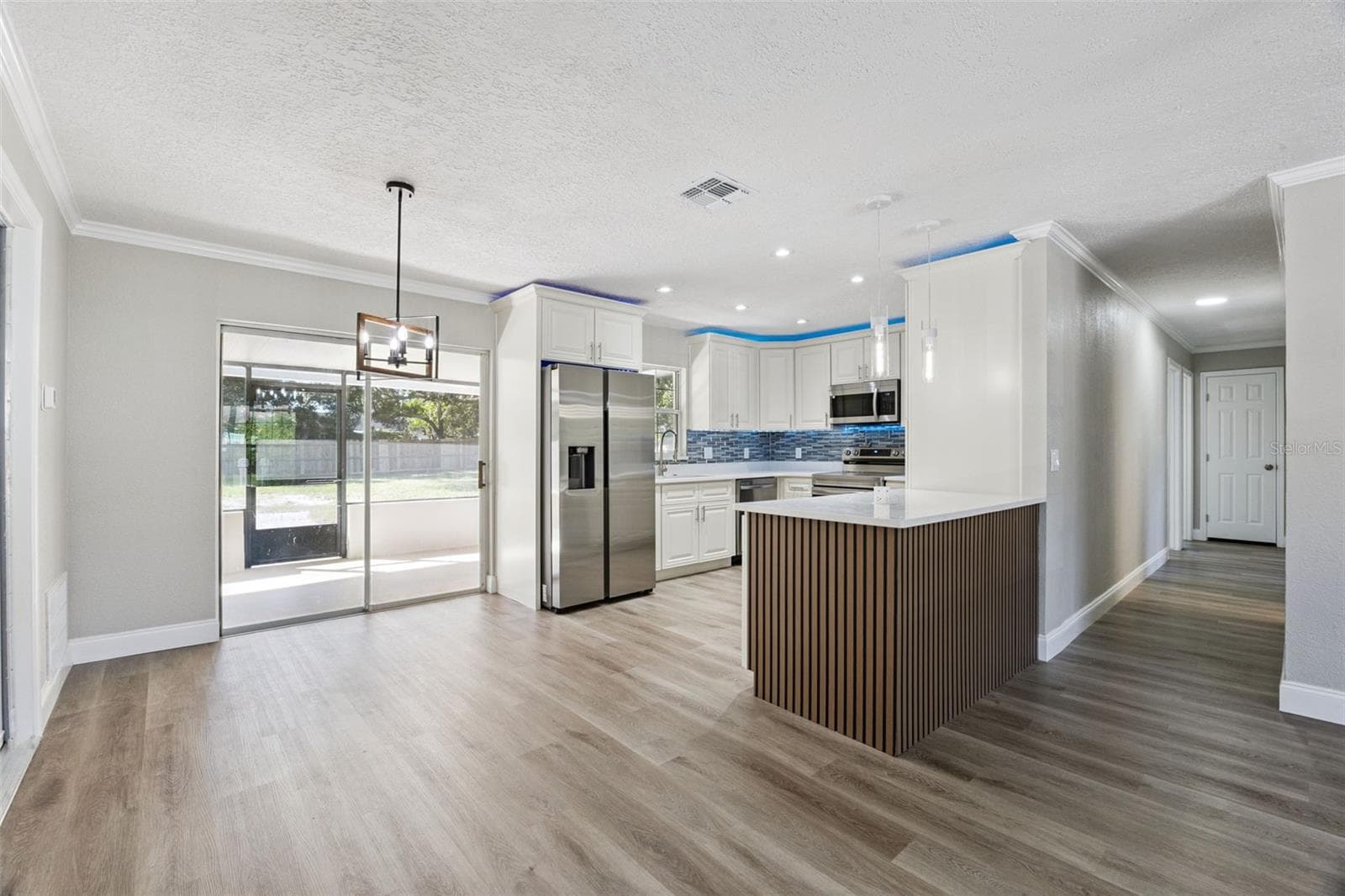 Kitchen & Hallway Overview: Updated kitchen complete with white cabinetry, ambient blue LED accent lighting, tile backsplash, stainless steel appliances, and island peninsula seating. - 720 GEORGIA AVE, LONGWOOD