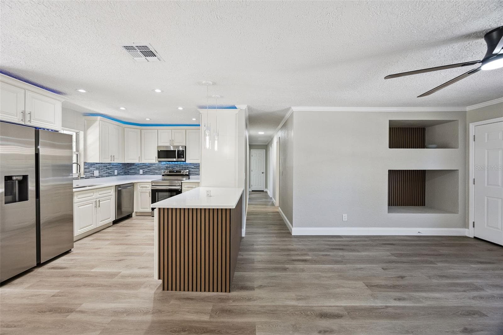 Open Living & Kitchen Layout: Expansive view of the open living space and kitchen, highlighting luxury vinyl plank flooring, custom wood-slat island bar, and built-in wall display niches. - 720 GEORGIA AVE, LONGWOOD