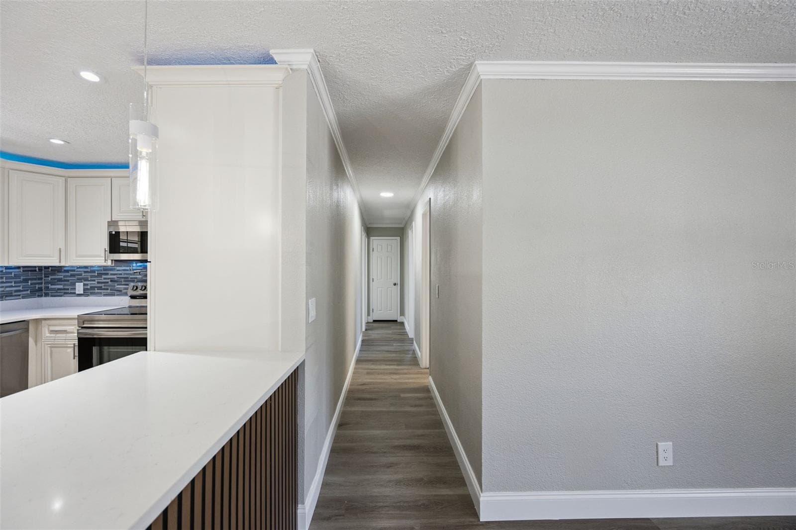 Central Hallway Corridor: Bright central hallway with luxury vinyl plank flooring, neutral paint, crown molding, and view past the custom slatted kitchen peninsula - 720 GEORGIA AVE, LONGWOOD