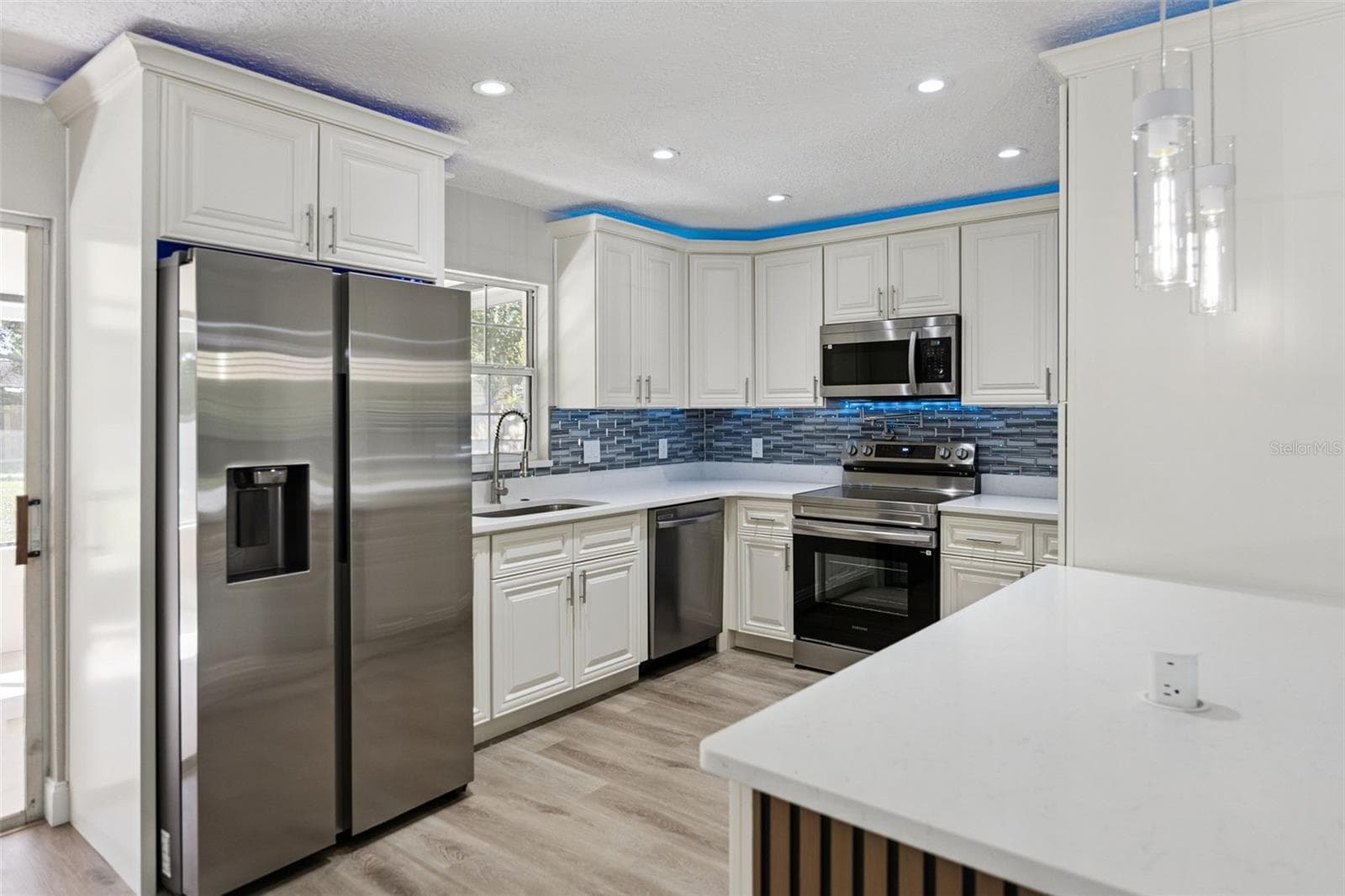 Gourmet Kitchen Corner: Upgraded kitchen perspective showcasing stainless steel appliances, raised-panel white cabinetry, quartz counters, and ambient ceiling lighting. - 720 GEORGIA AVE, LONGWOOD
