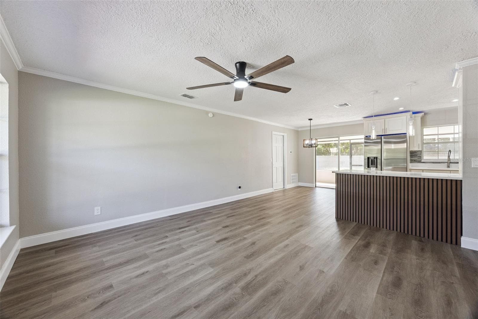 Living Room to Kitchen View: Expansive main living room highlighting fresh neutral tones, modern ceiling fan, and a custom wood-slat kitchen peninsula. - 720 GEORGIA AVE, LONGWOOD