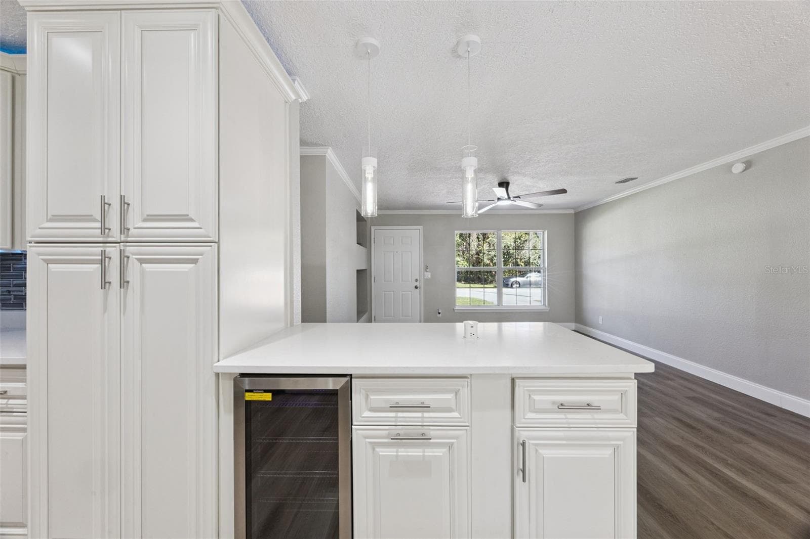 Island Peninsula & Wine Cooler: Close-up view of the kitchen peninsula bar equipped with an under-counter wine fridge, quartz counter overhang, and sleek pendant lighting. - 720 GEORGIA AVE, LONGWOOD
